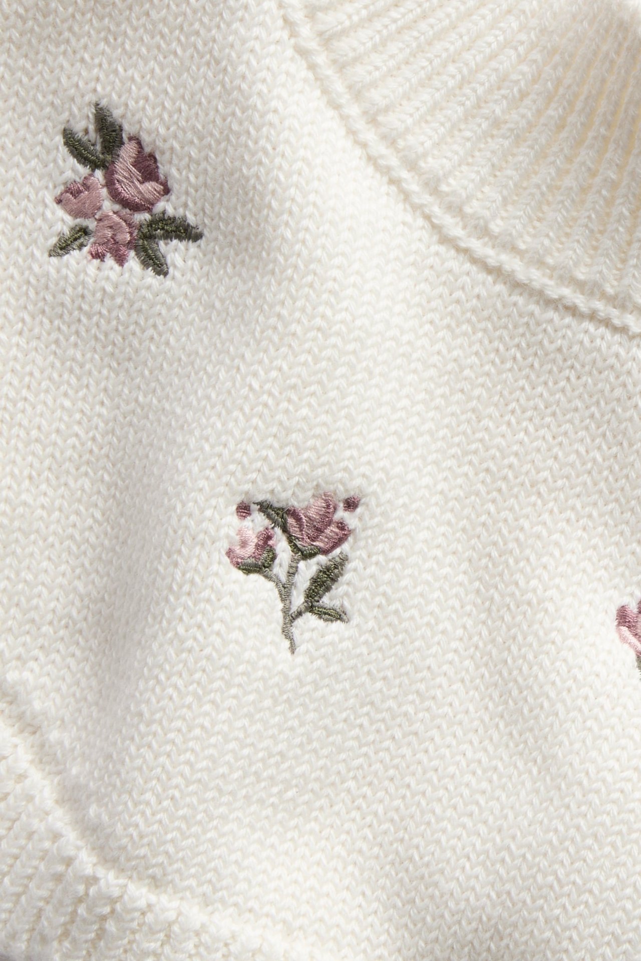Nahaufnahme eines weißen Strickpullovers mit rosa Blumenstickerei.