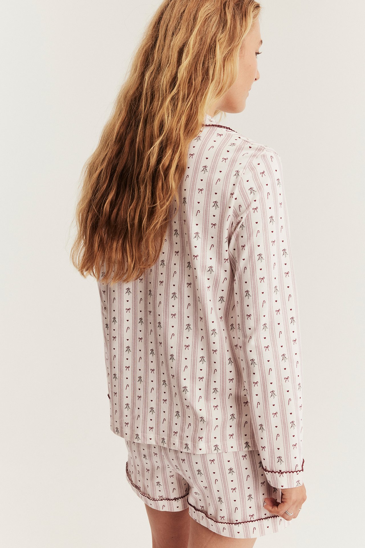 Back view of a woman wearing a white and maroon striped pajama set with candy cane and bow print.