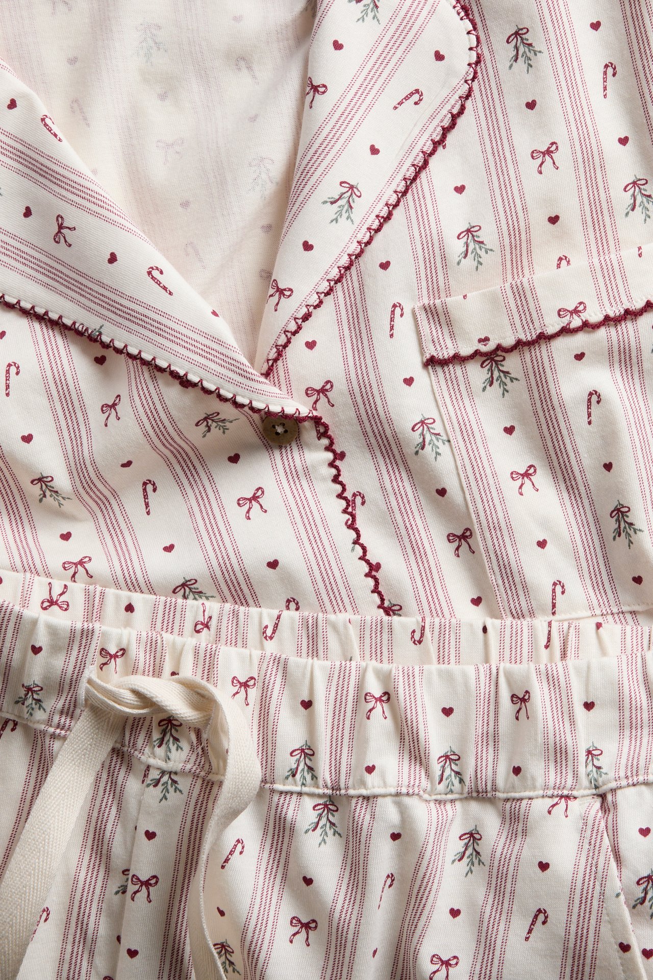Nahaufnahme eines creme-rot gestreiften Pyjama-Sets mit Herz-, Schleifen-, Zuckerstangen- und Misteldruck.