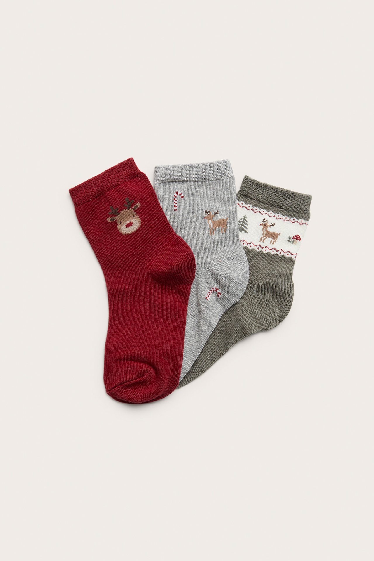 Nahaufnahme von drei Paar Weihnachtssocken: eine rote mit Rentier, eine graue mit Zuckerstangen und eine grüne mit Rentier-Muster.