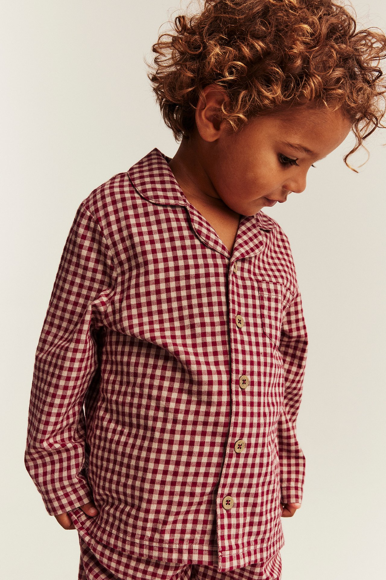 Front view of a kid wearing a red and beige checked pajama shirt with matching pants.