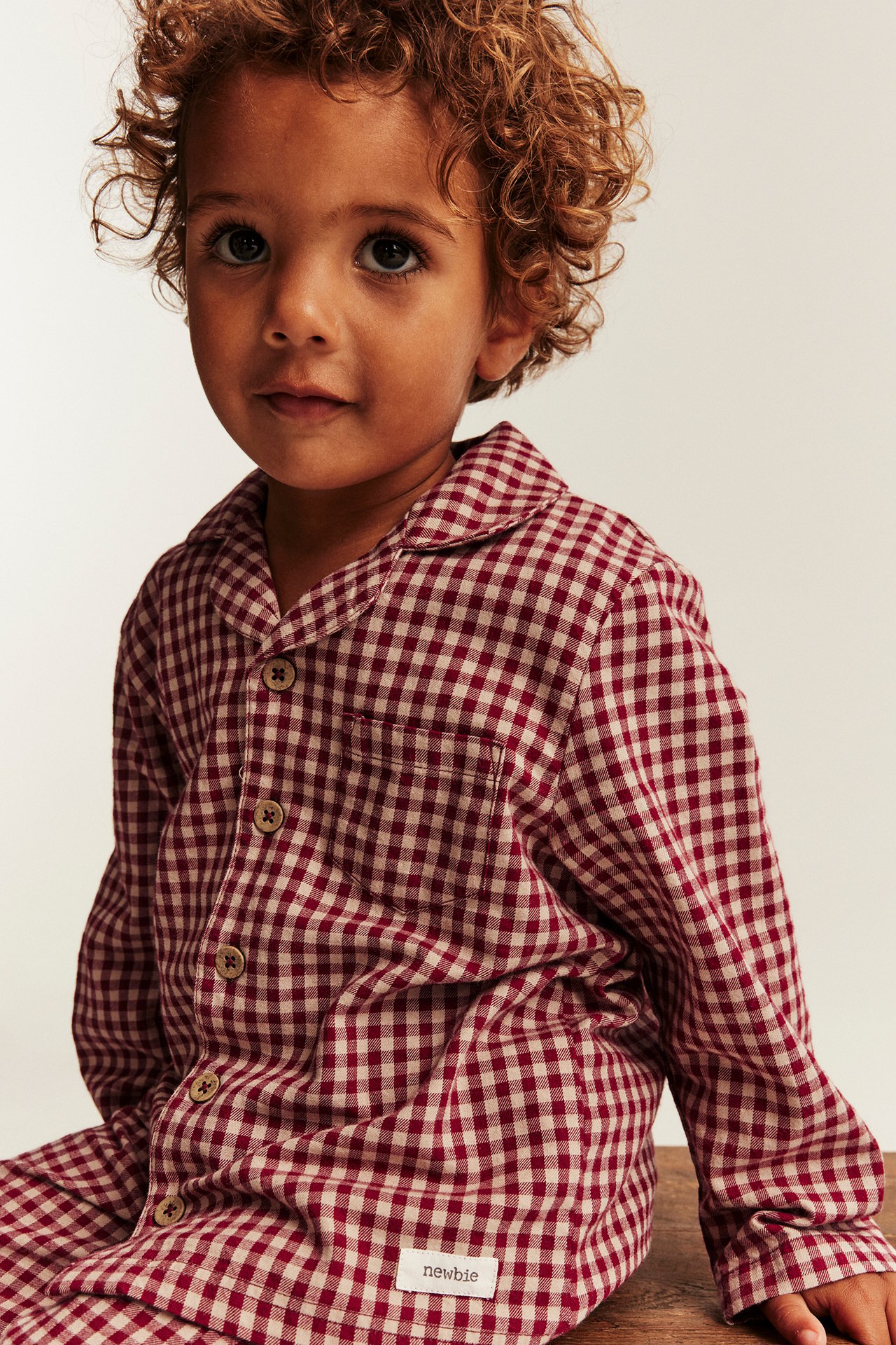 Front view of a kid in a red and beige checkered pajama top with buttons and a chest pocket.