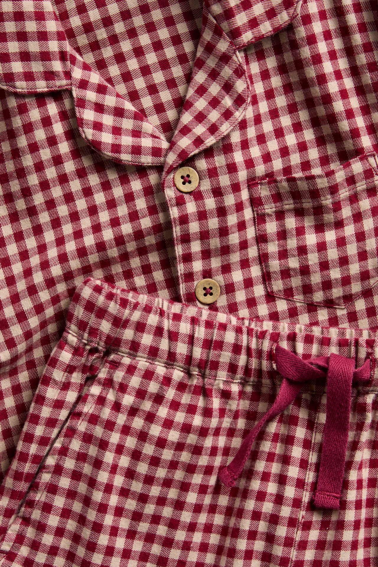 Nahaufnahme eines rot-weiß karierten Flanell-Pyjamas mit Holzknöpfen und Kordelzug.
