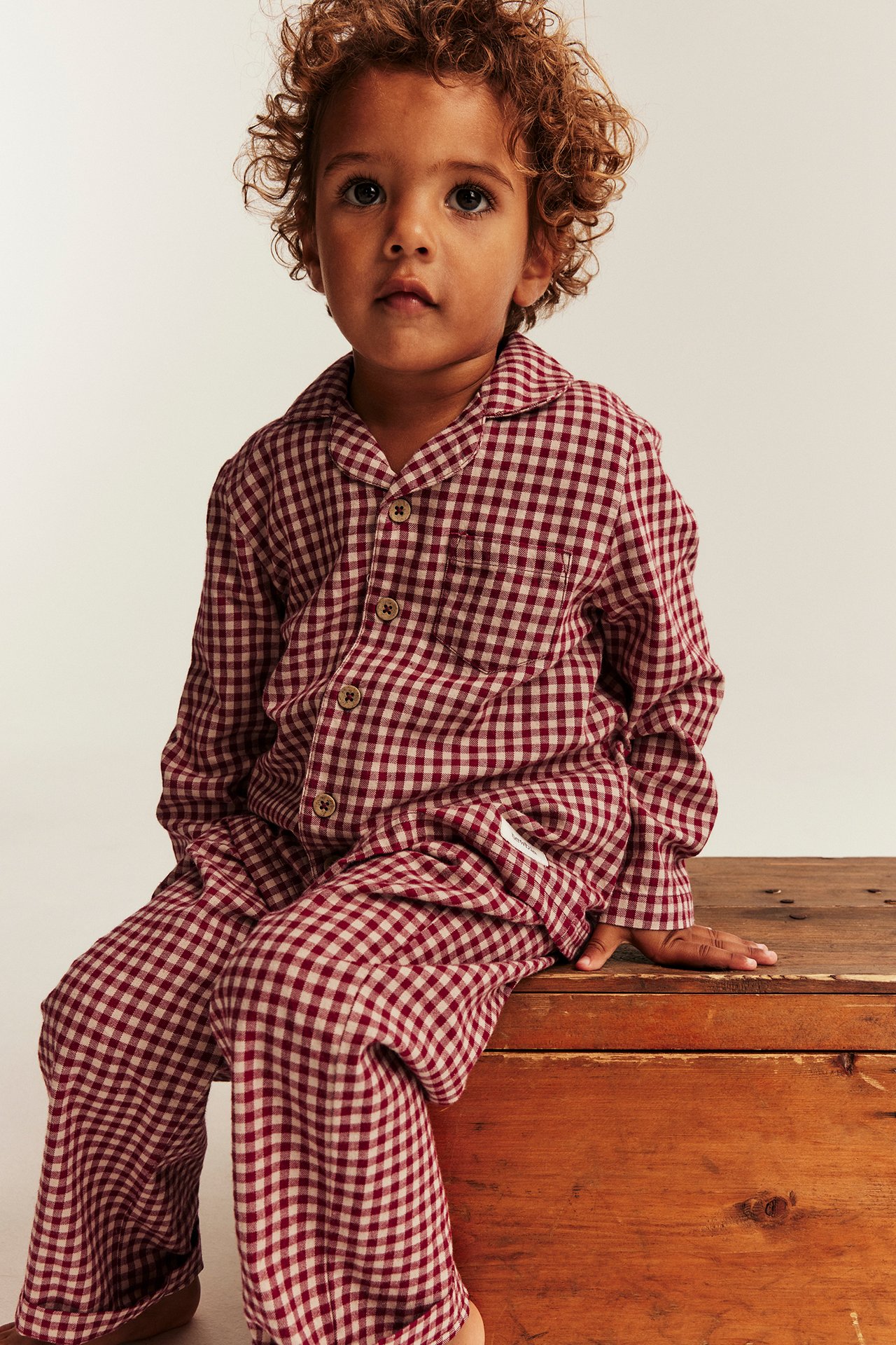 Front view of a kid wearing red and beige gingham checked pajamas.