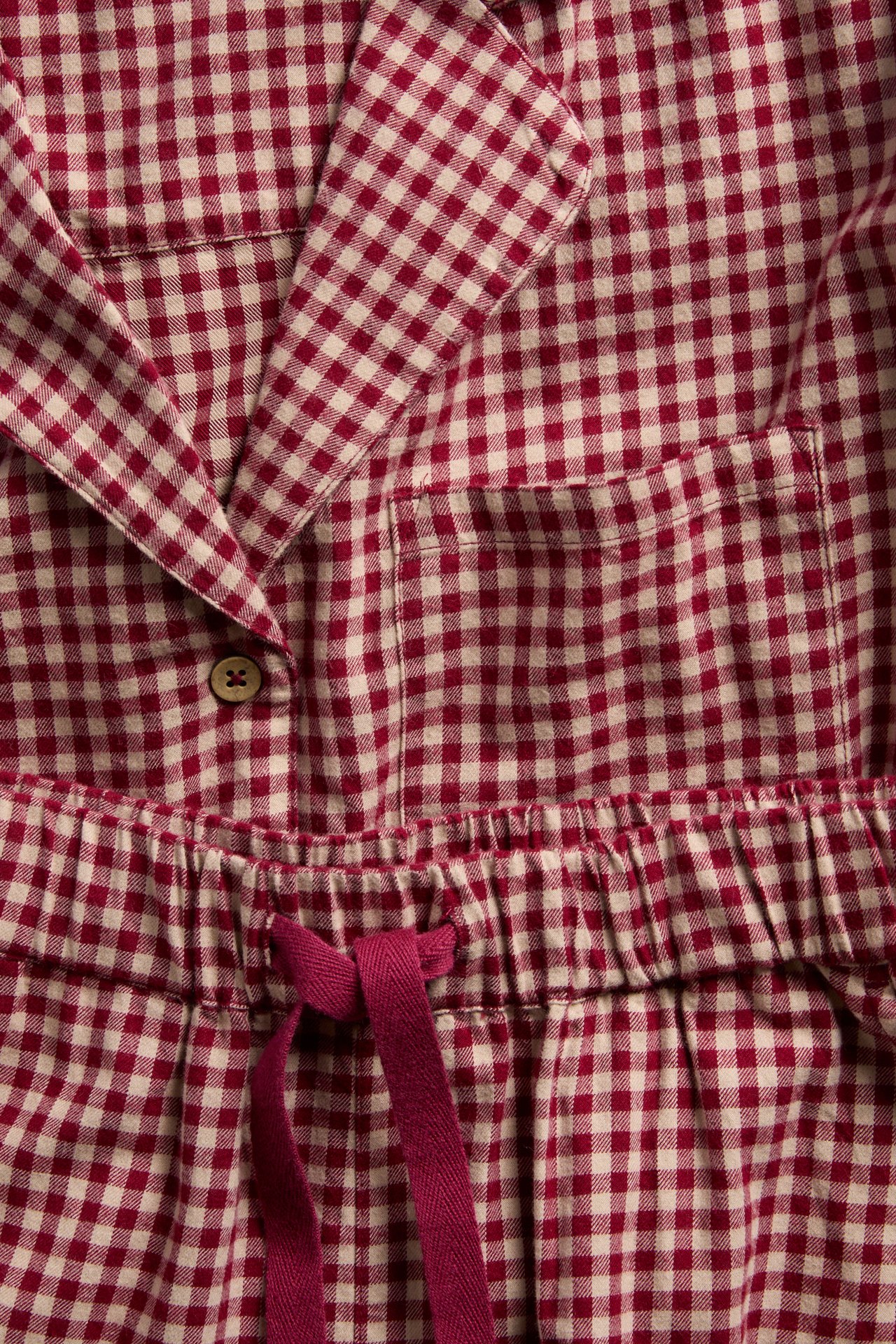Close-up: Red and cream gingham pajama set with collar, button, chest pocket, and drawstring waist.
