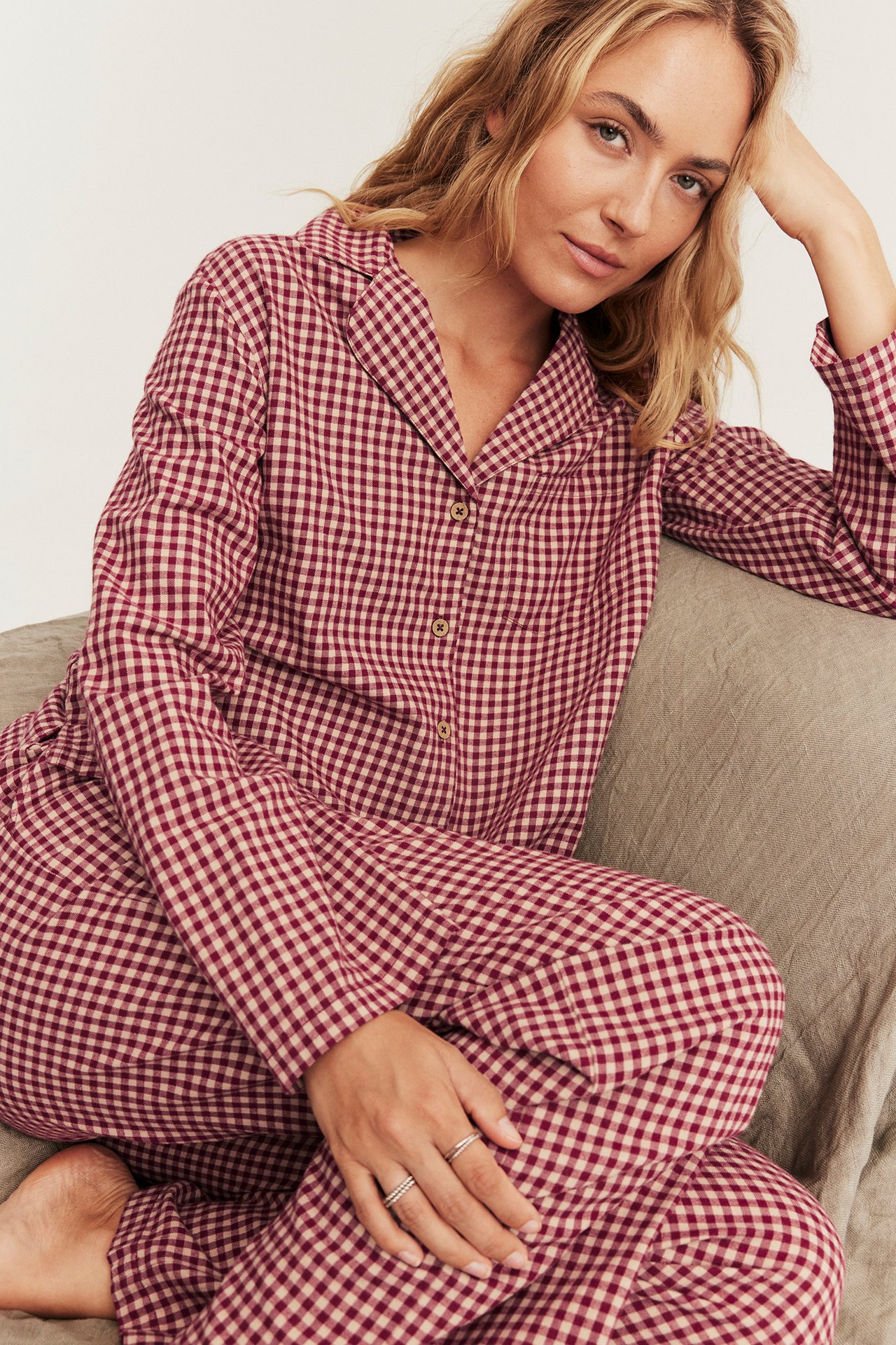 Front view of a woman wearing a maroon and beige gingham pajama set with two rings.