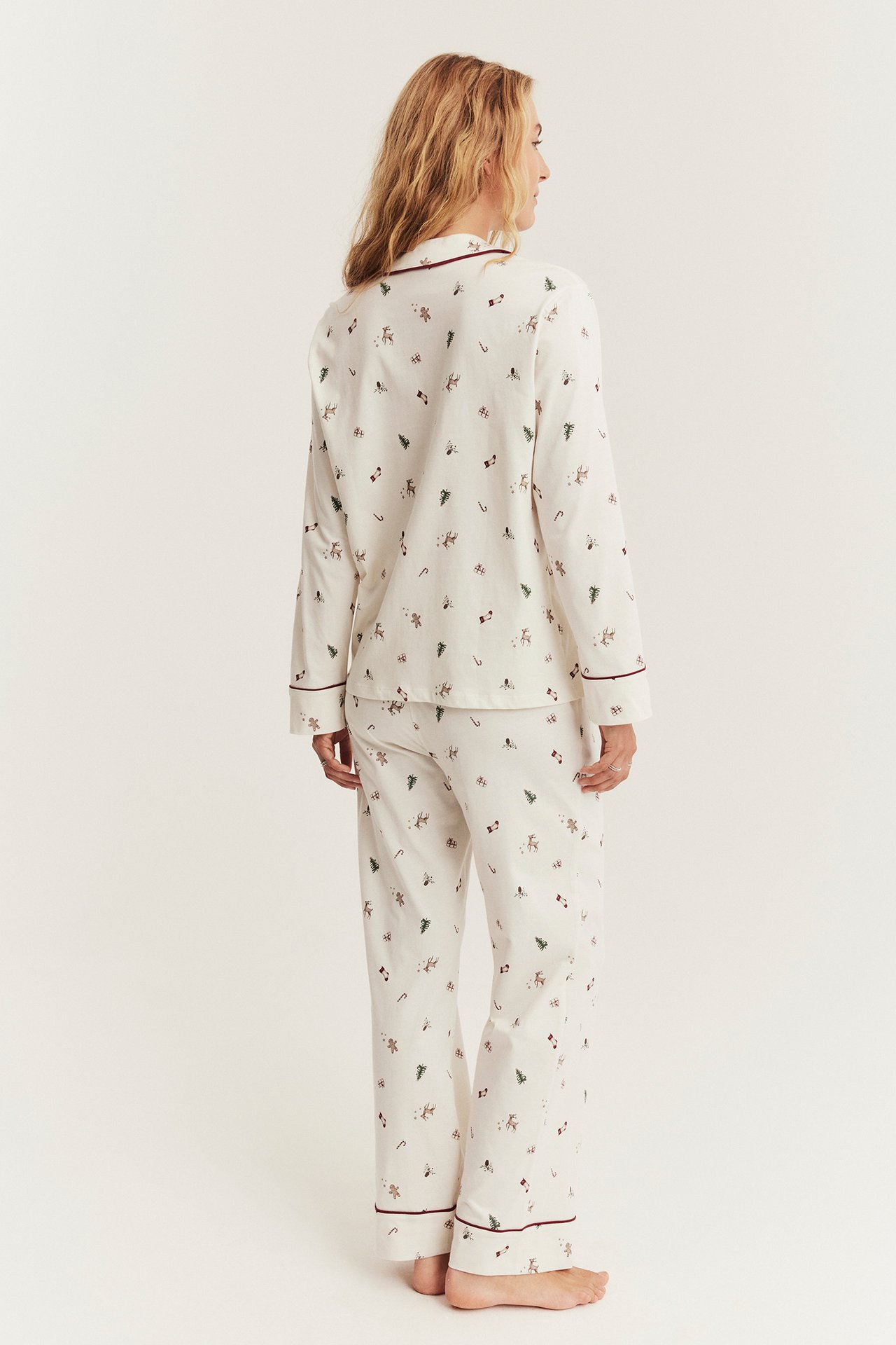 Rückenansicht einer Frau in cremefarbenem Pyjama mit Weihnachtsmuster und bordeauxroten Paspeln.