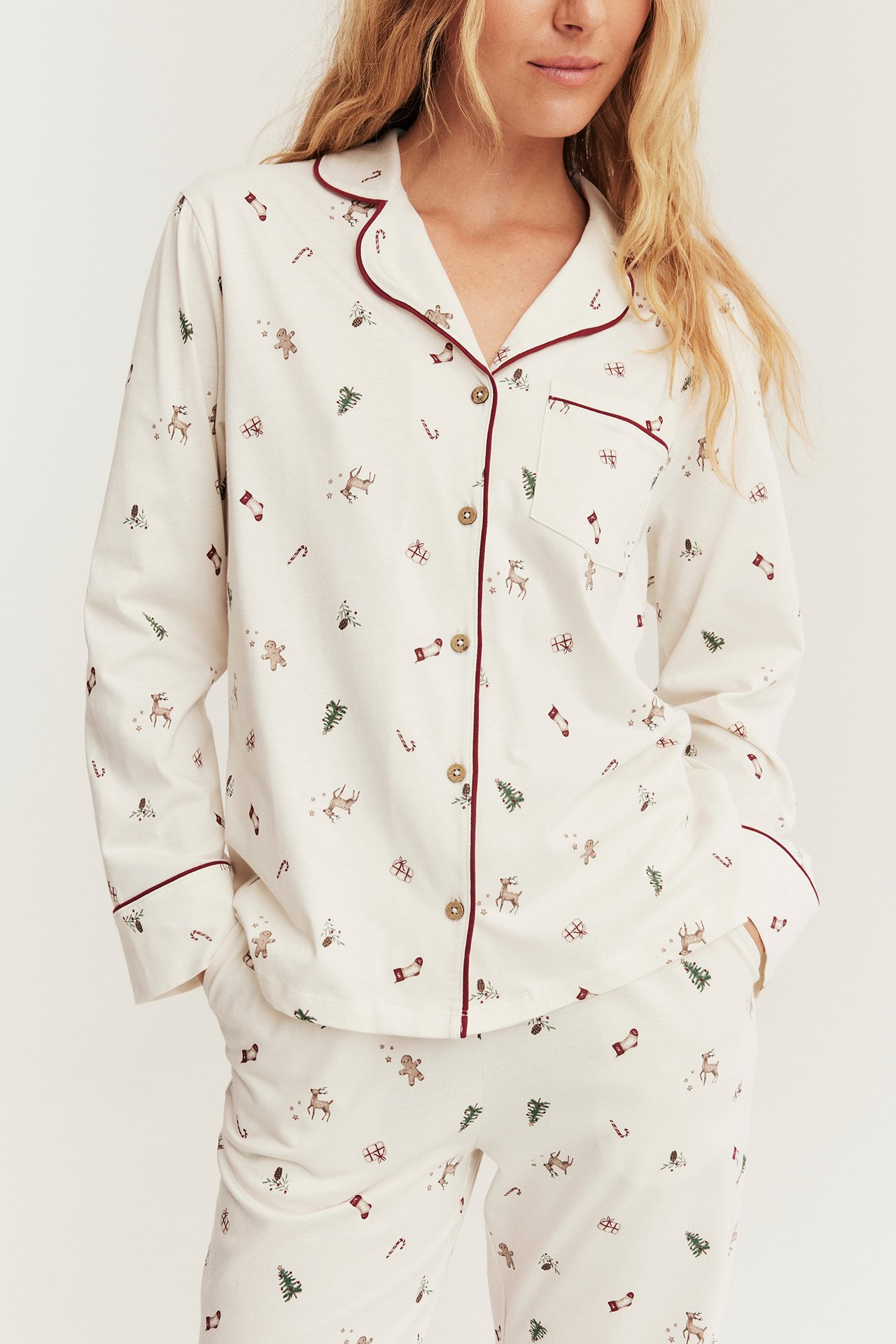 Vorderansicht einer Frau in einem weißen Pyjama-Set mit Weihnachtsmuster und roter Paspel.