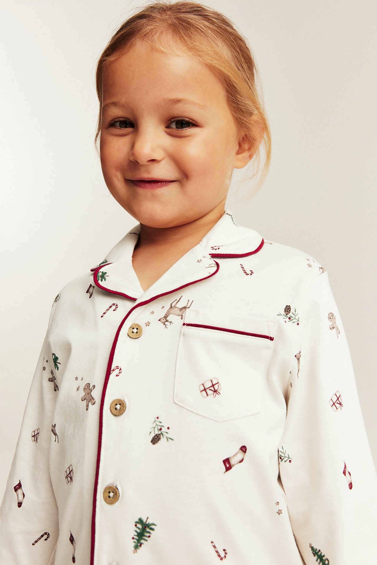 Weißes Kinder-Pyjamaoberteil mit Weihnachtsdruck und roter Paspel, Vorderansicht.