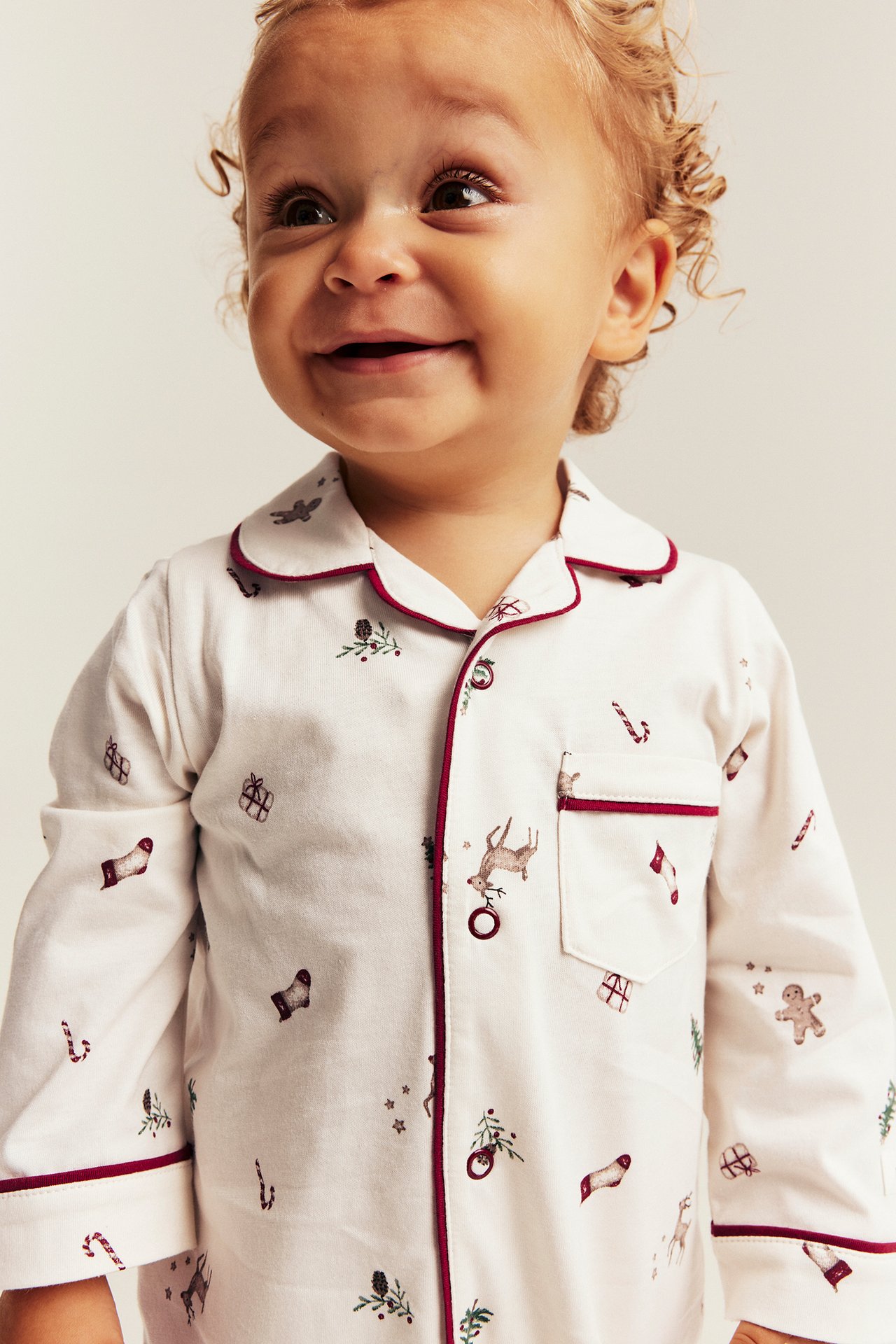 Close-up of a baby wearing an off-white Christmas-print pajama top with red piping and buttons.