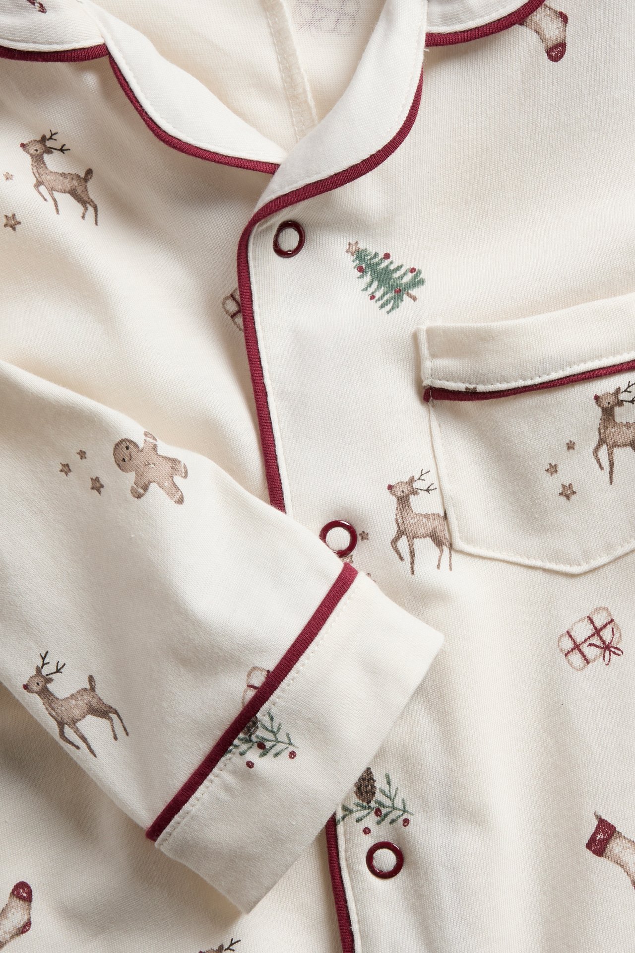 Close-up of a kid's off-white pajama top with red piping and Christmas print.