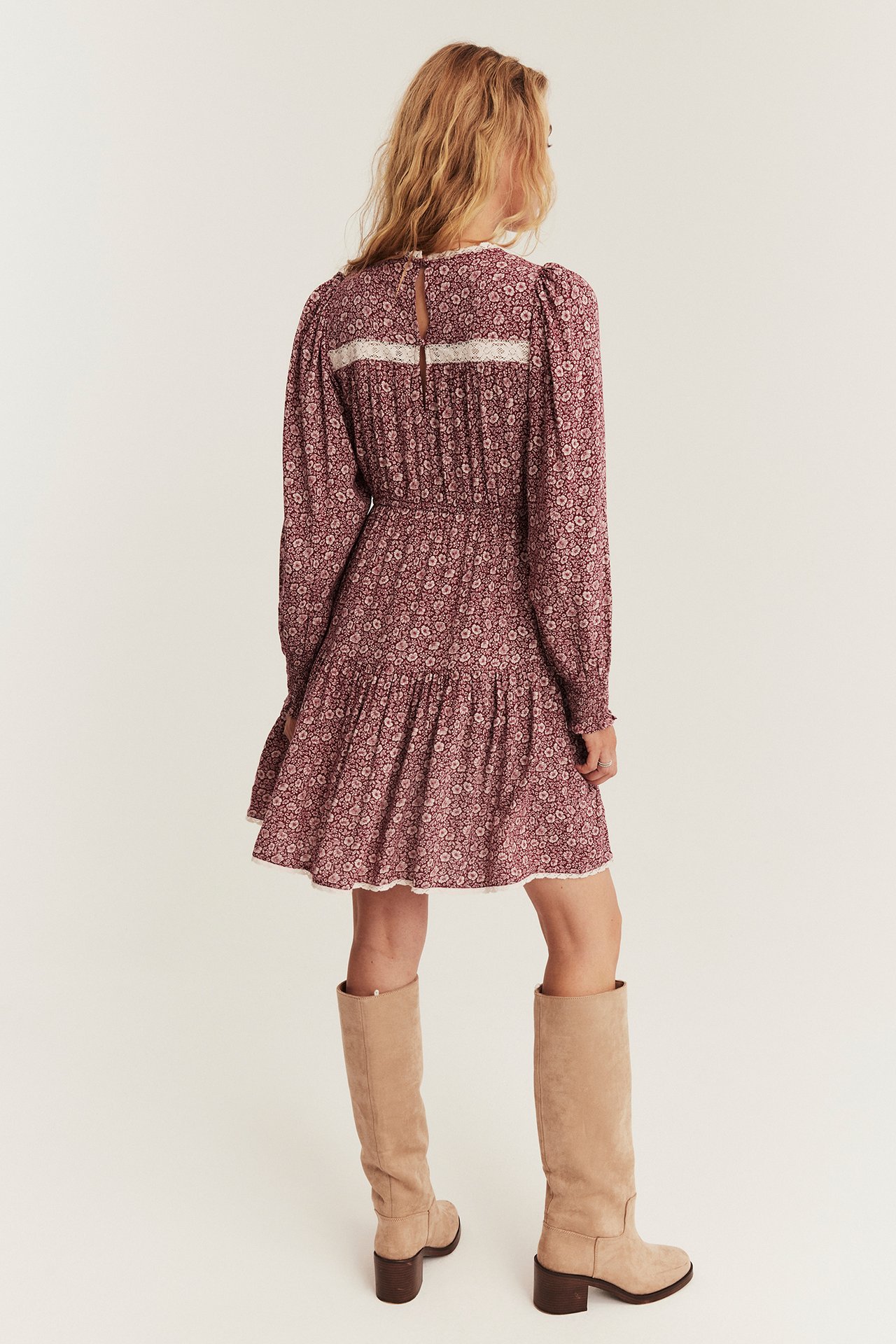 Woman's back view, maroon floral print dress with lace trim, paired with beige knee boots.