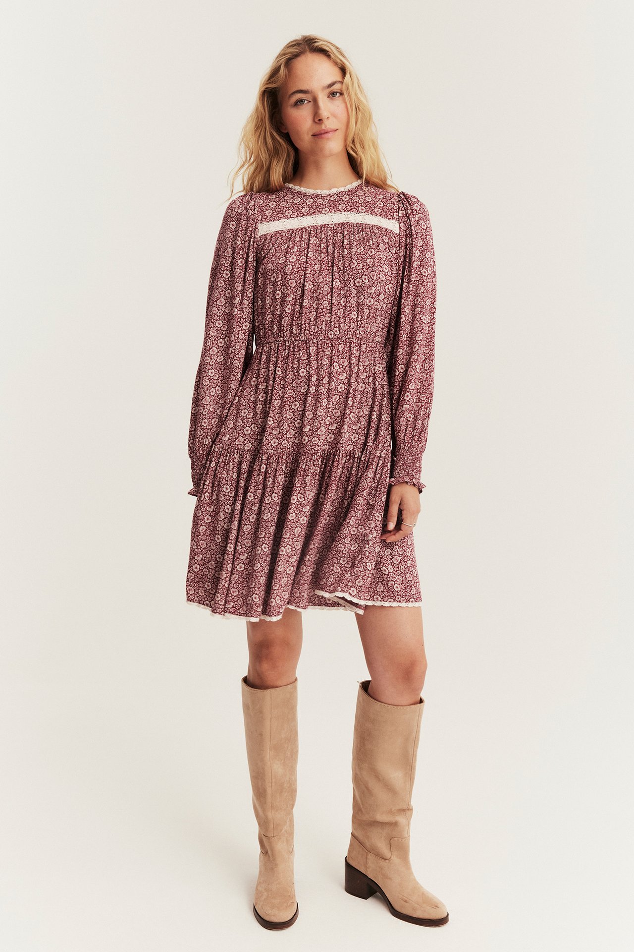 Vorderansicht: Damen rotes Blumenmuster langärmeliges Minikleid mit weißer Spitzenborte, kombiniert mit hohen beigen Stiefeln.