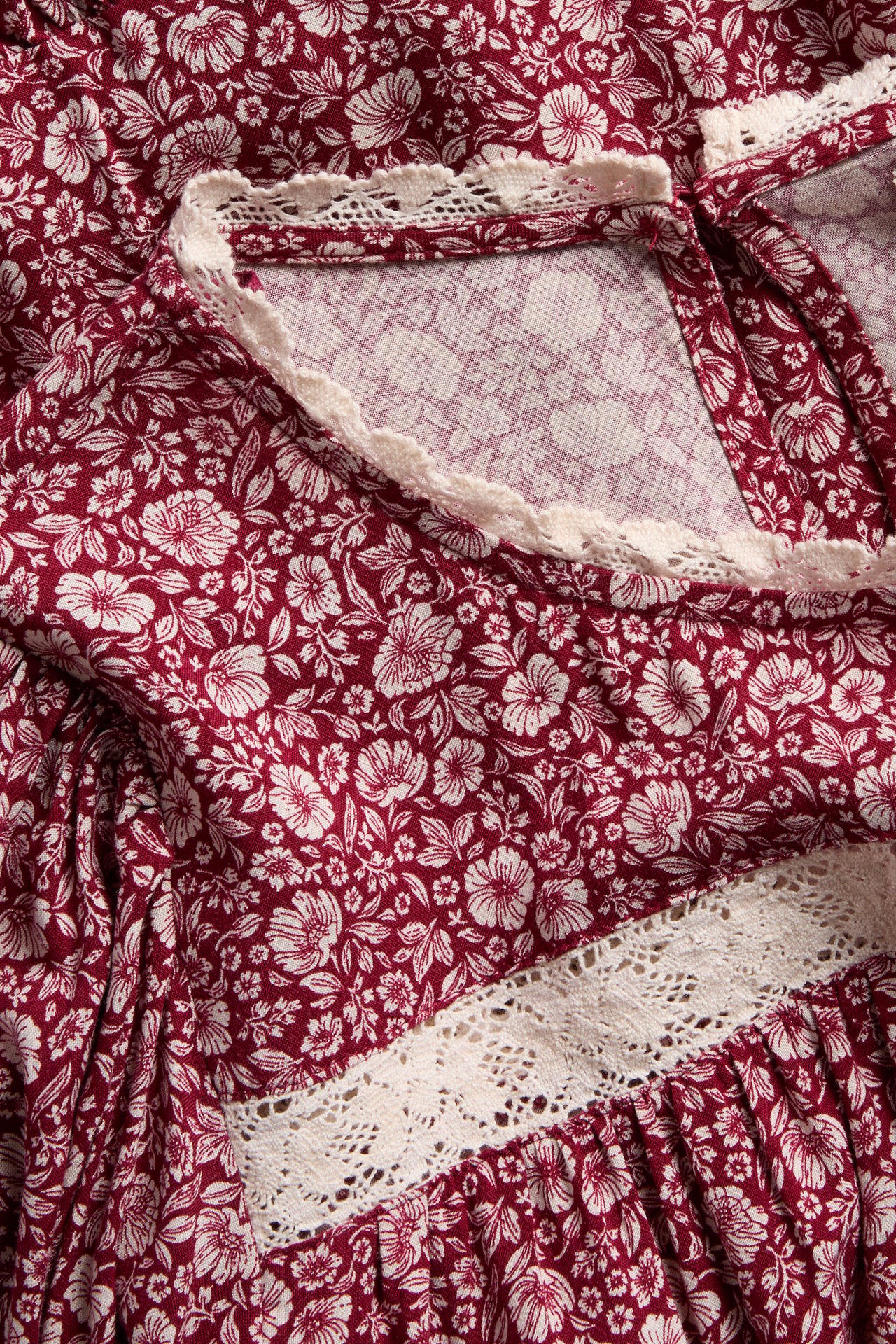 Close-up of a red floral dress with white floral print and cream lace trim.