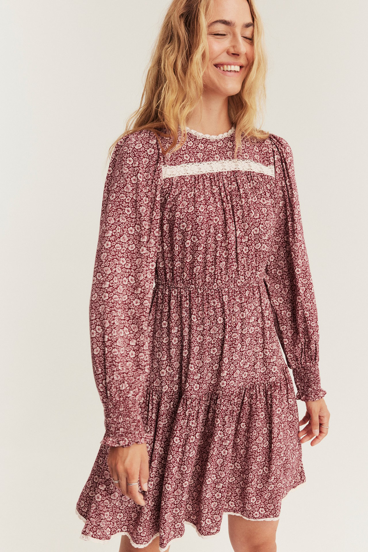 Front view of a smiling woman wearing a maroon floral tiered mini-dress with lace trim.