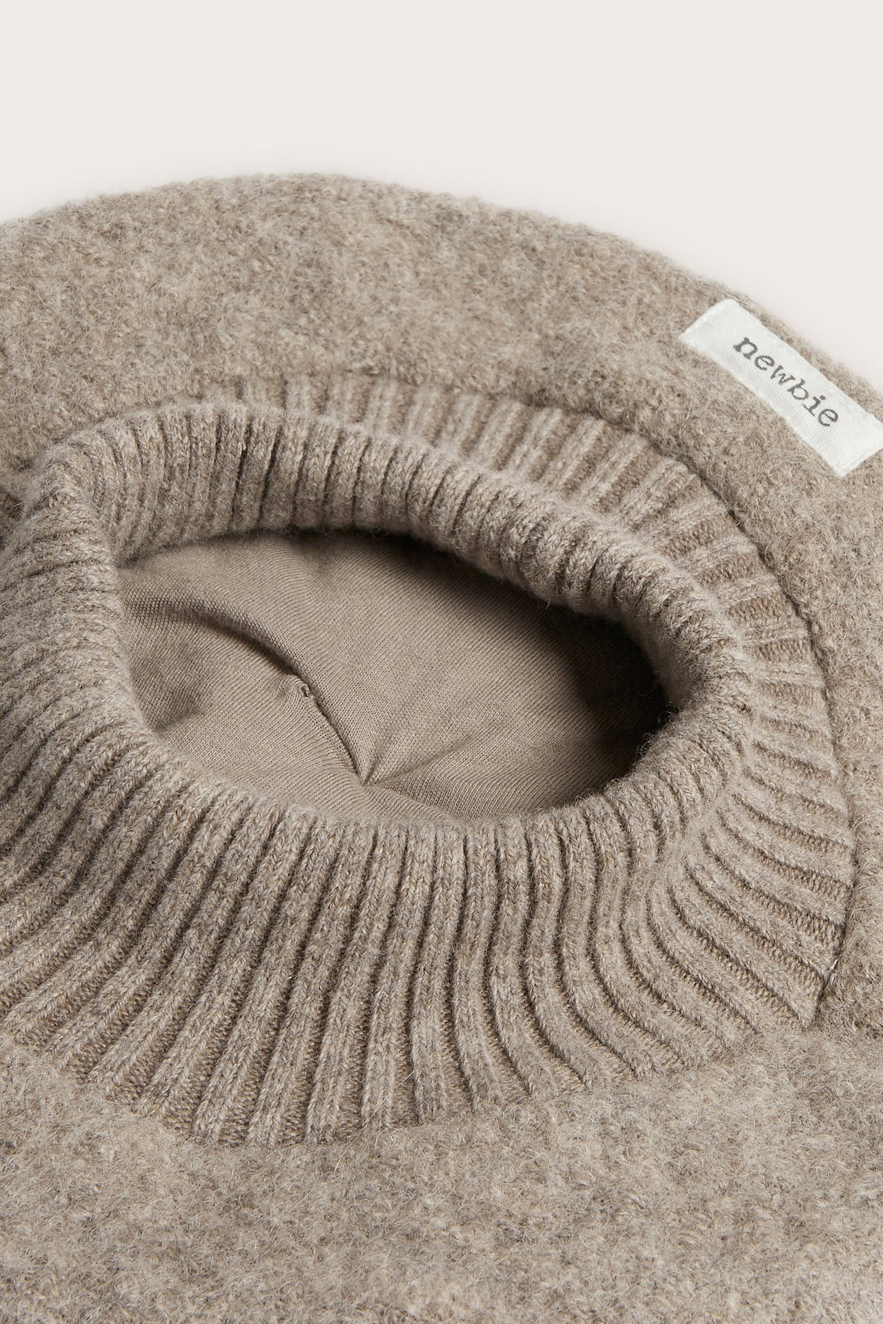 Nahaufnahme eines hellbraunen flauschigen Strickoberteils mit geripptem Ausschnitt.