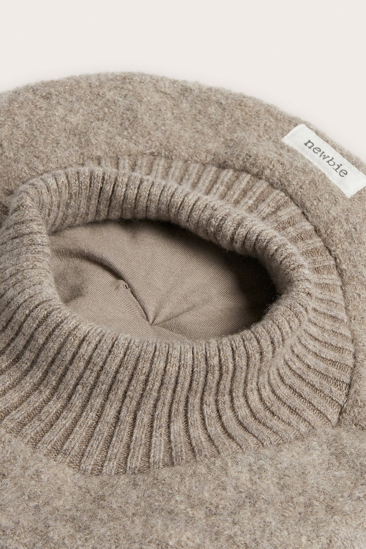 Nahaufnahme eines hellbraunen flauschigen Strickoberteils mit geripptem Ausschnitt.