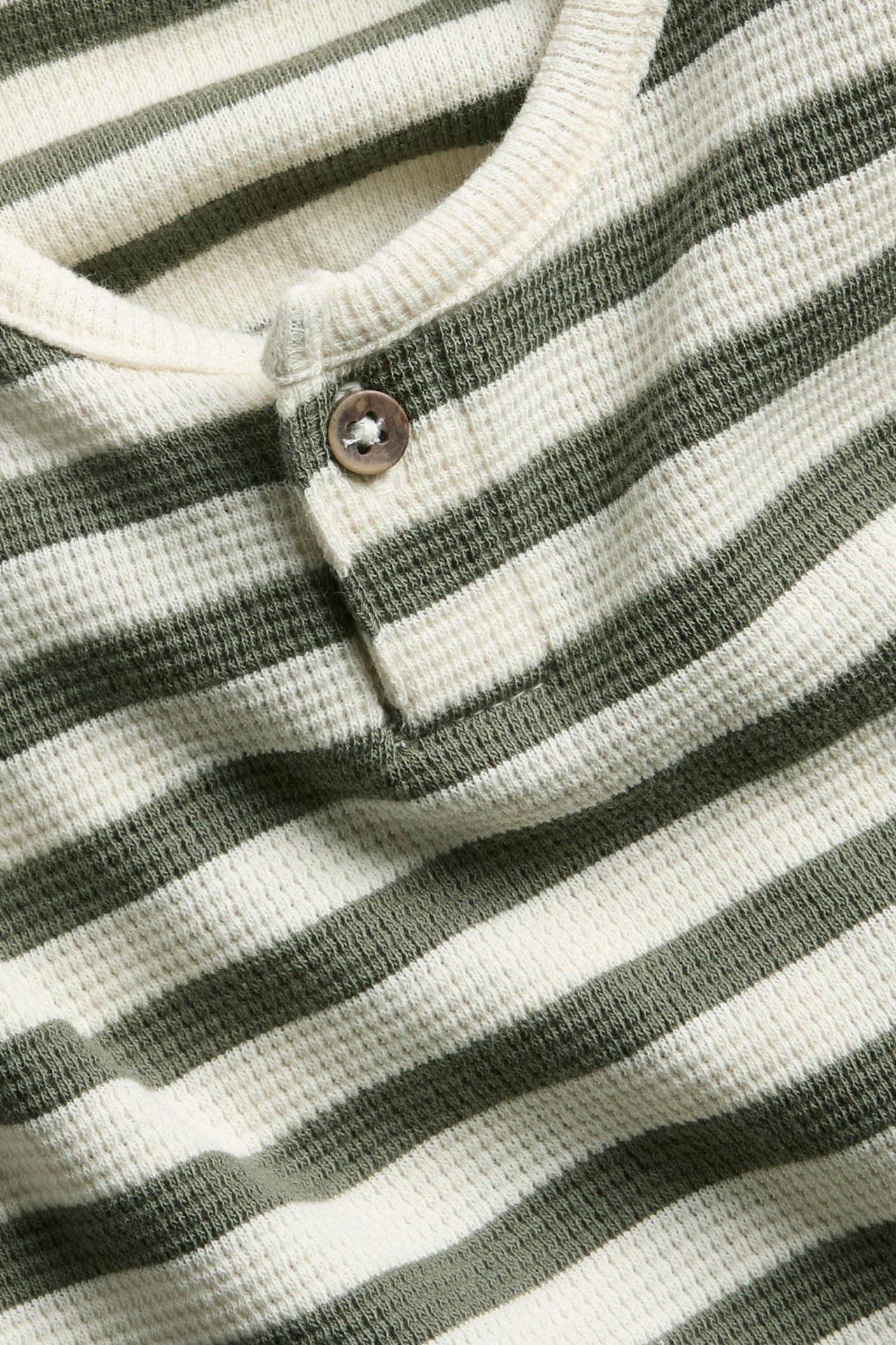 Nahaufnahme eines gestreiften Waffel-Langarmshirts in Creme und Dunkelgrün mit einem Knopf vorne.