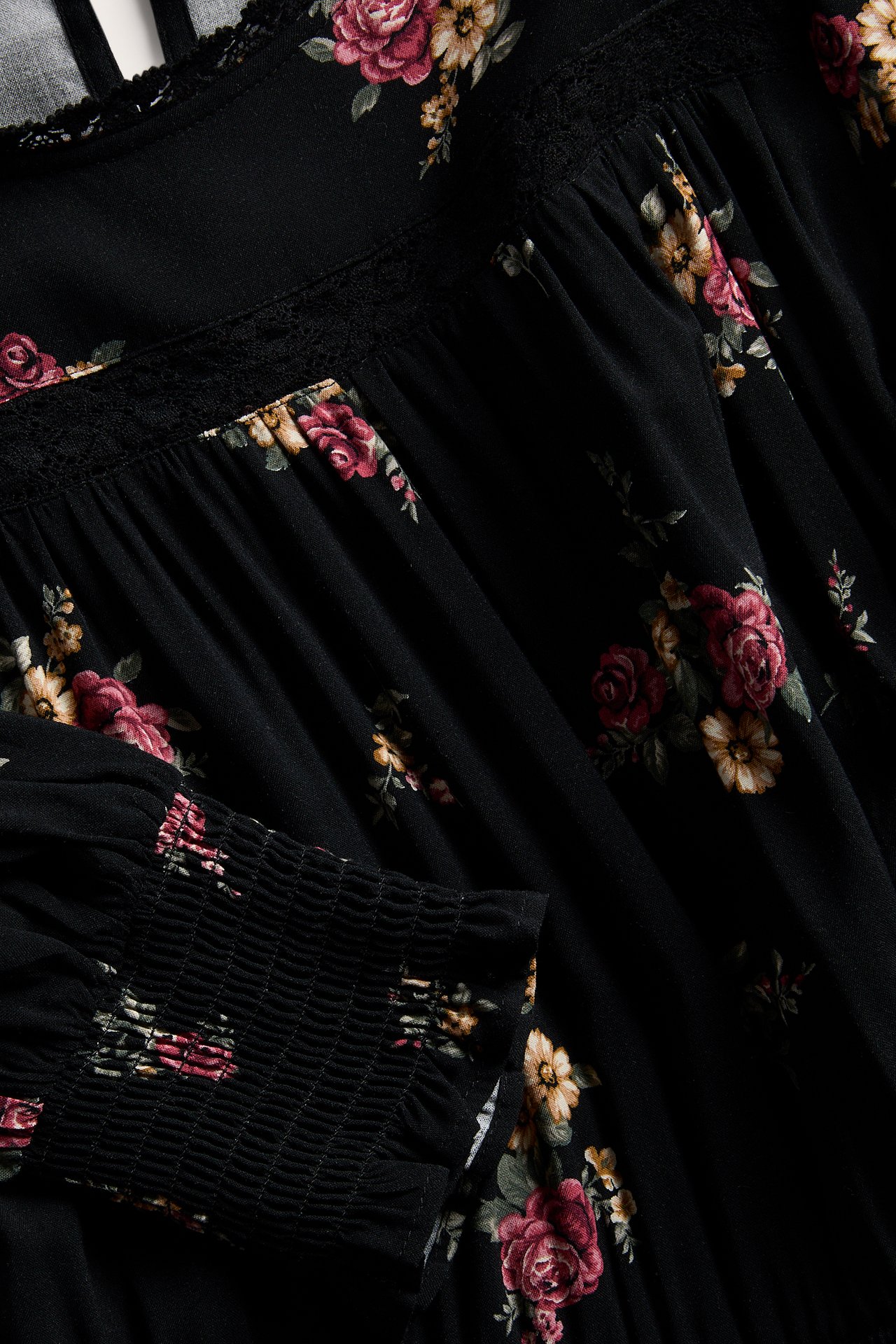 Nahaufnahme eines schwarzen floralen Kleides mit Spitzendetails und gesmokten Manschetten.