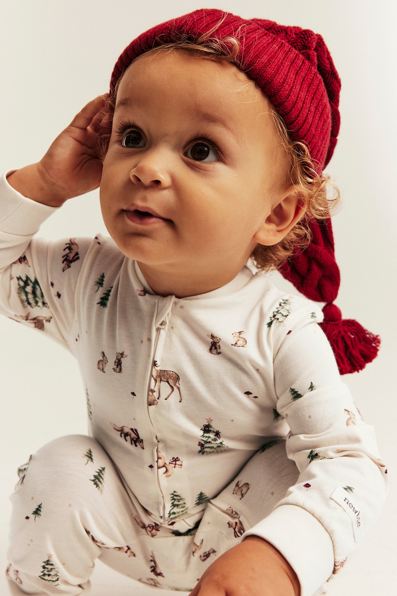 Close-up of baby in white forest print zip pajama and red ribbed knit beanie.
