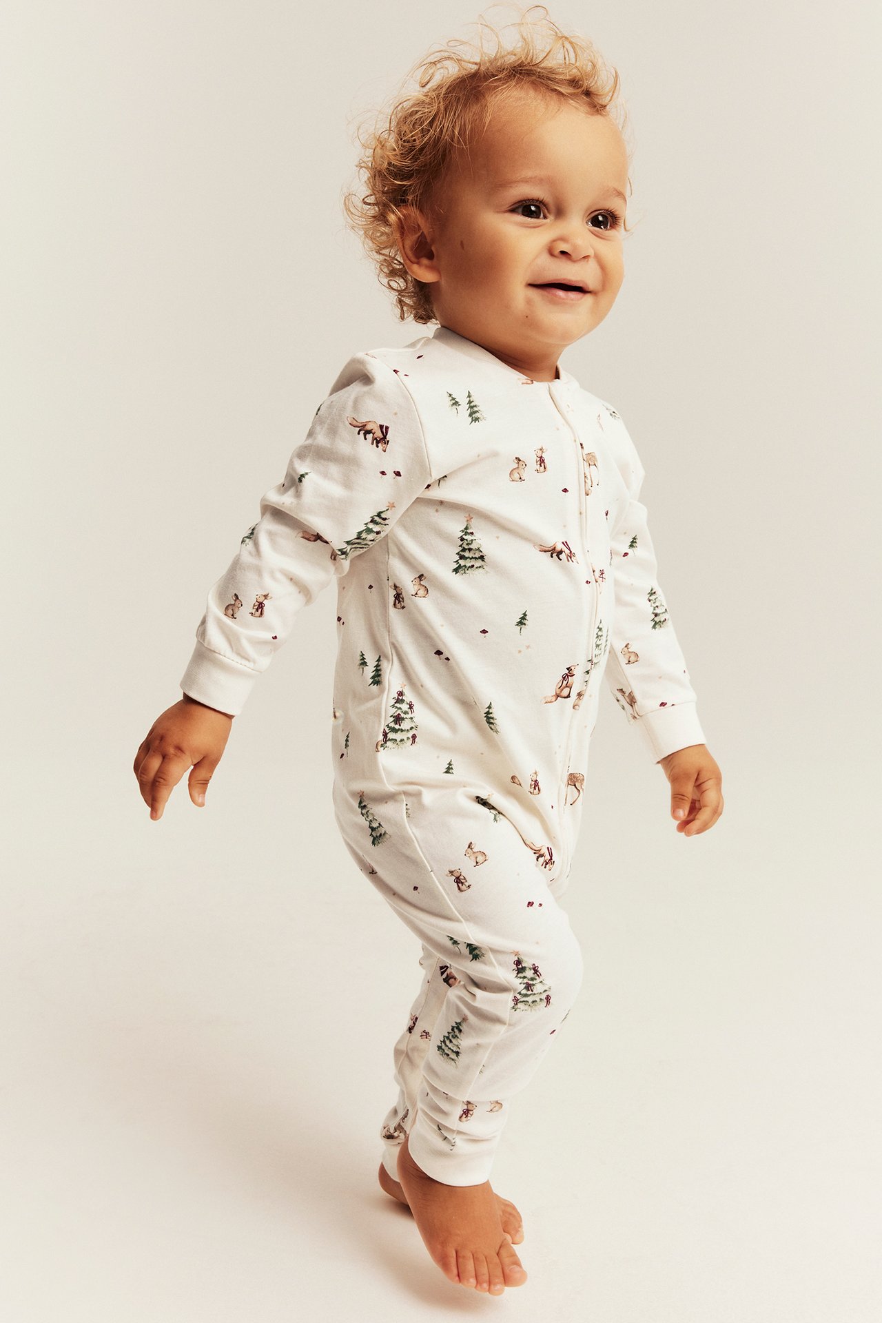 Side view of a baby wearing a white long-sleeved romper with a forest animal and tree print.