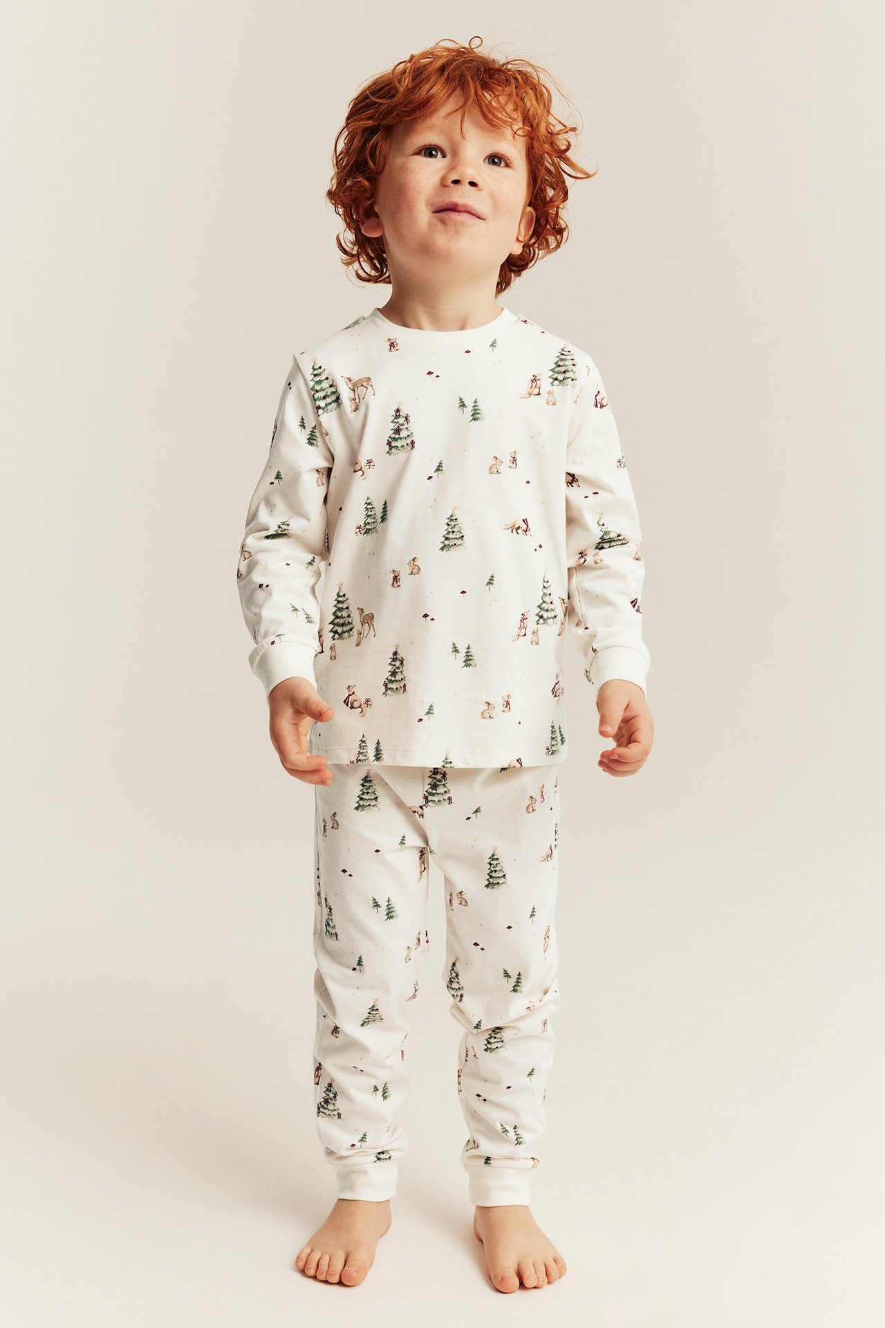 Front view of a kid wearing white pajamas with a forest animal and tree print.