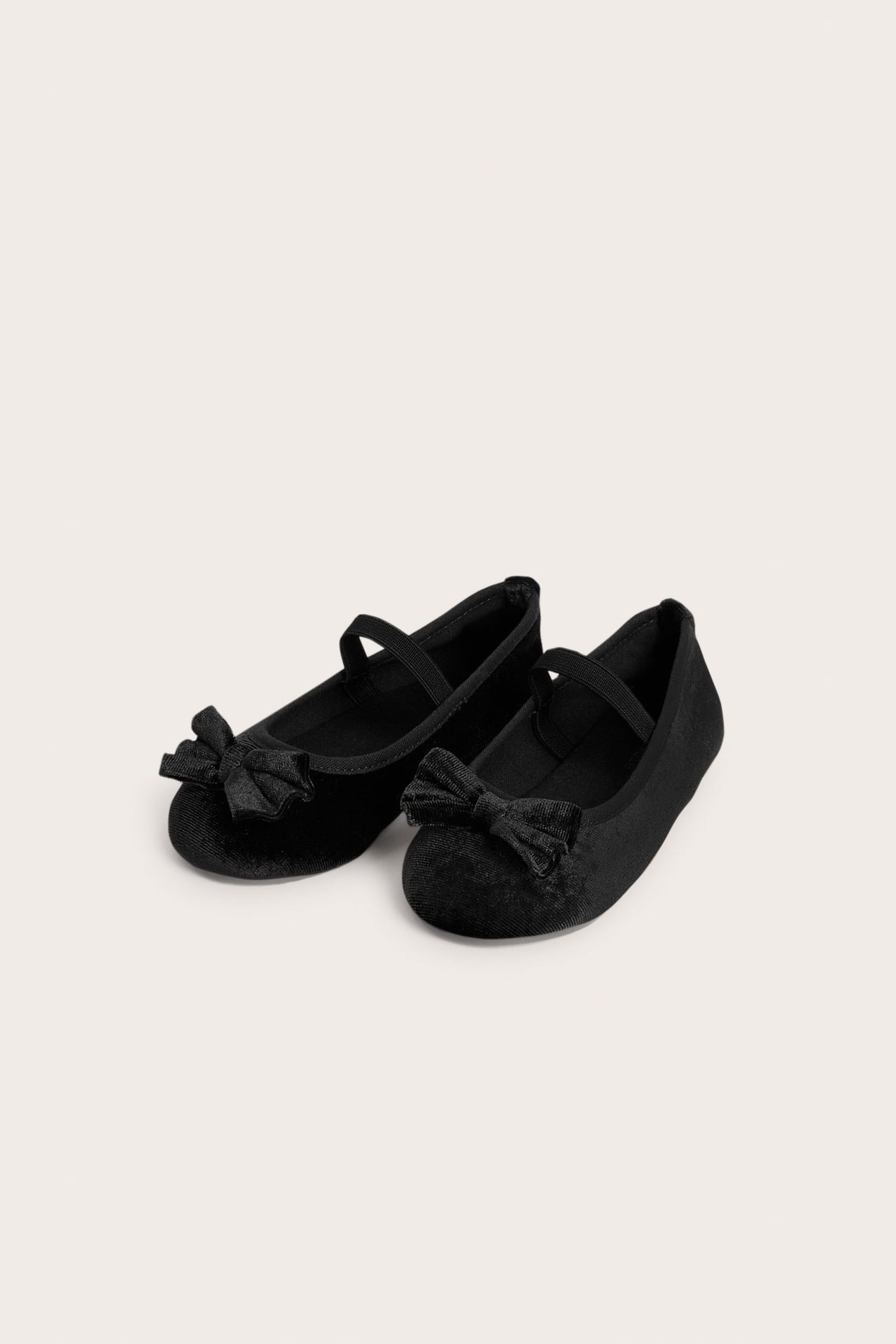 Draufsicht auf zwei schwarze Samt-Ballerinas für Kinder mit Schleifen und elastischen Riemen.