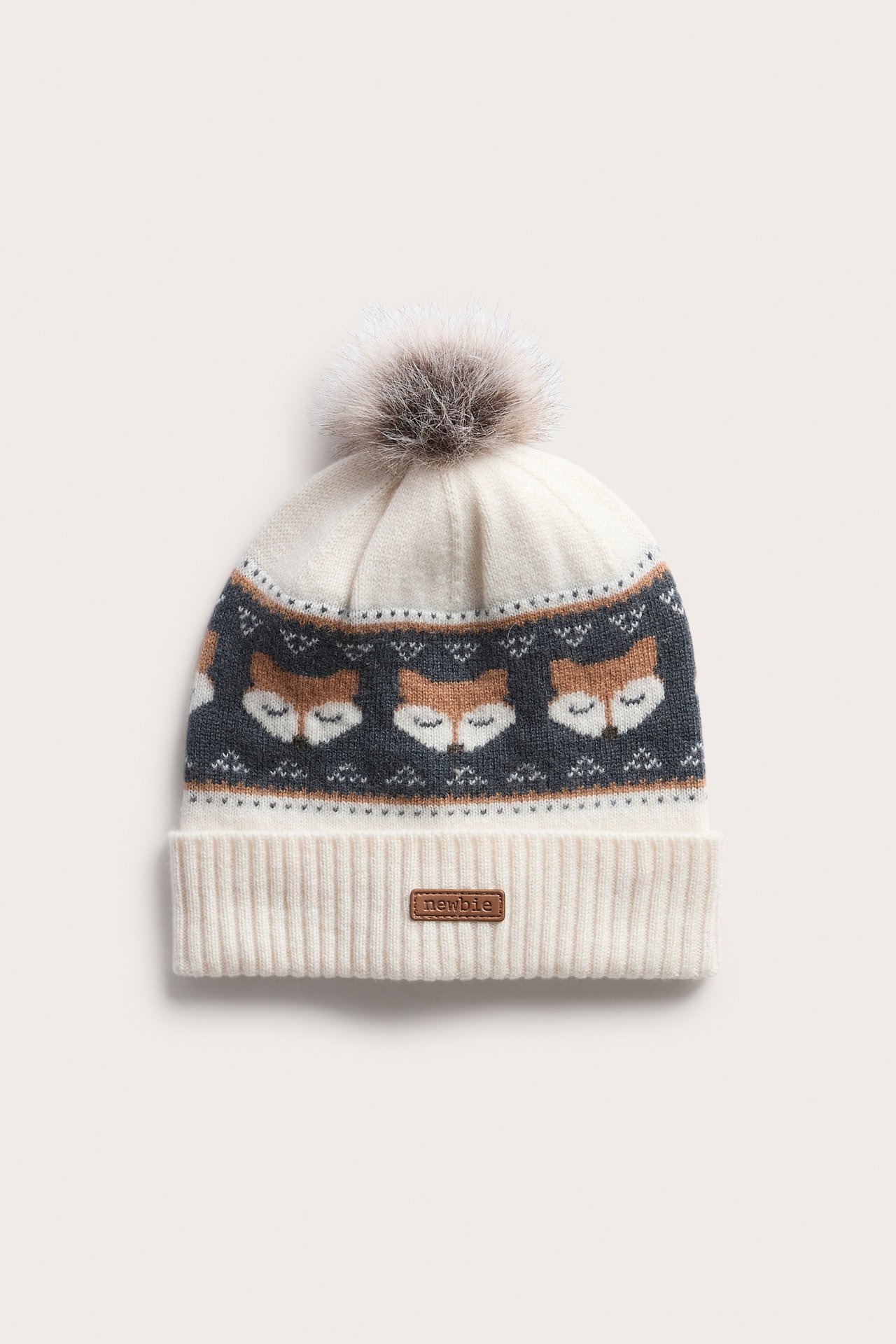 Vorderansicht einer cremefarbenen Strickmütze mit Fuchsmuster und braunem Bommel.