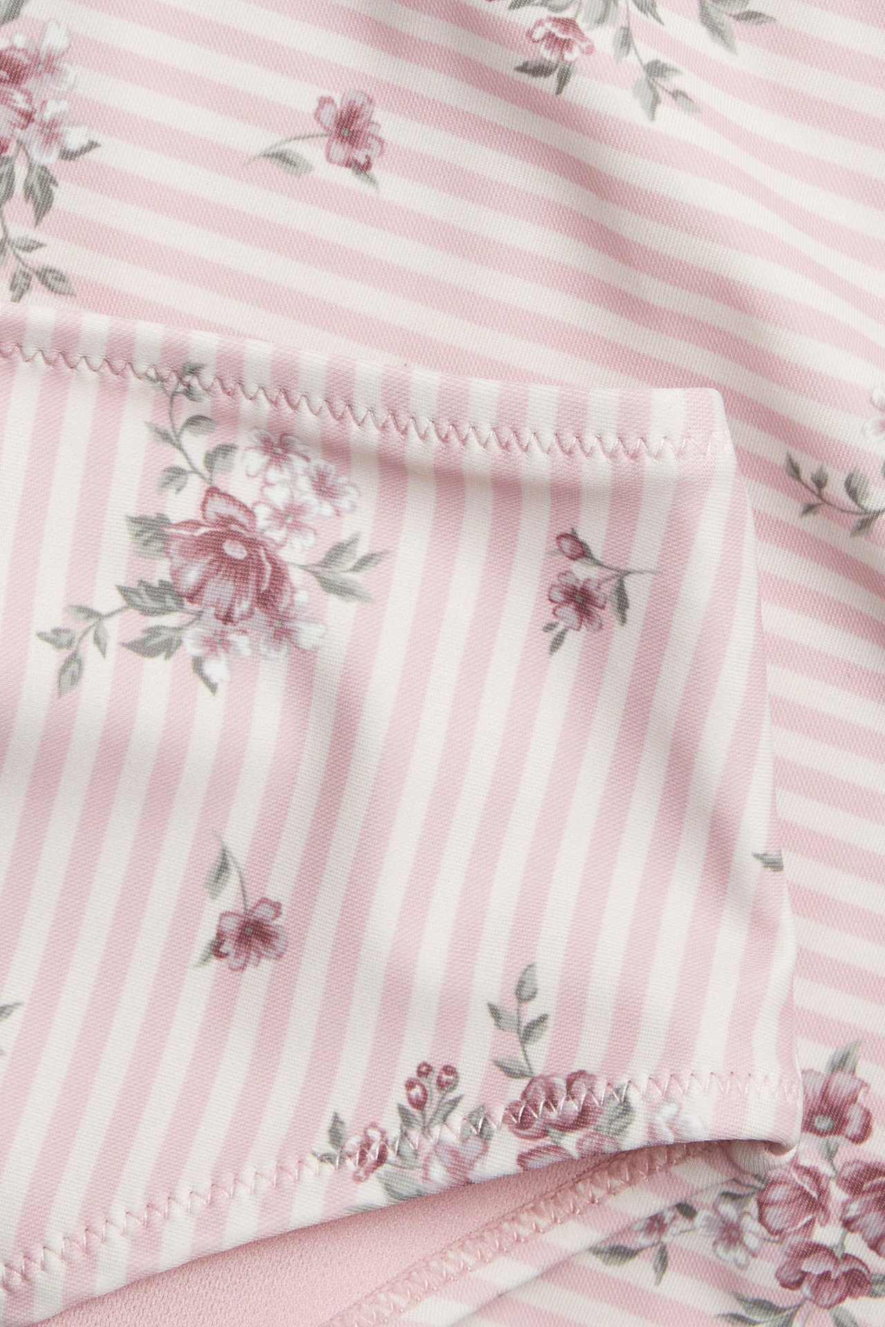 Close-up of a pink and white striped floral print garment with zig-zag stitching.