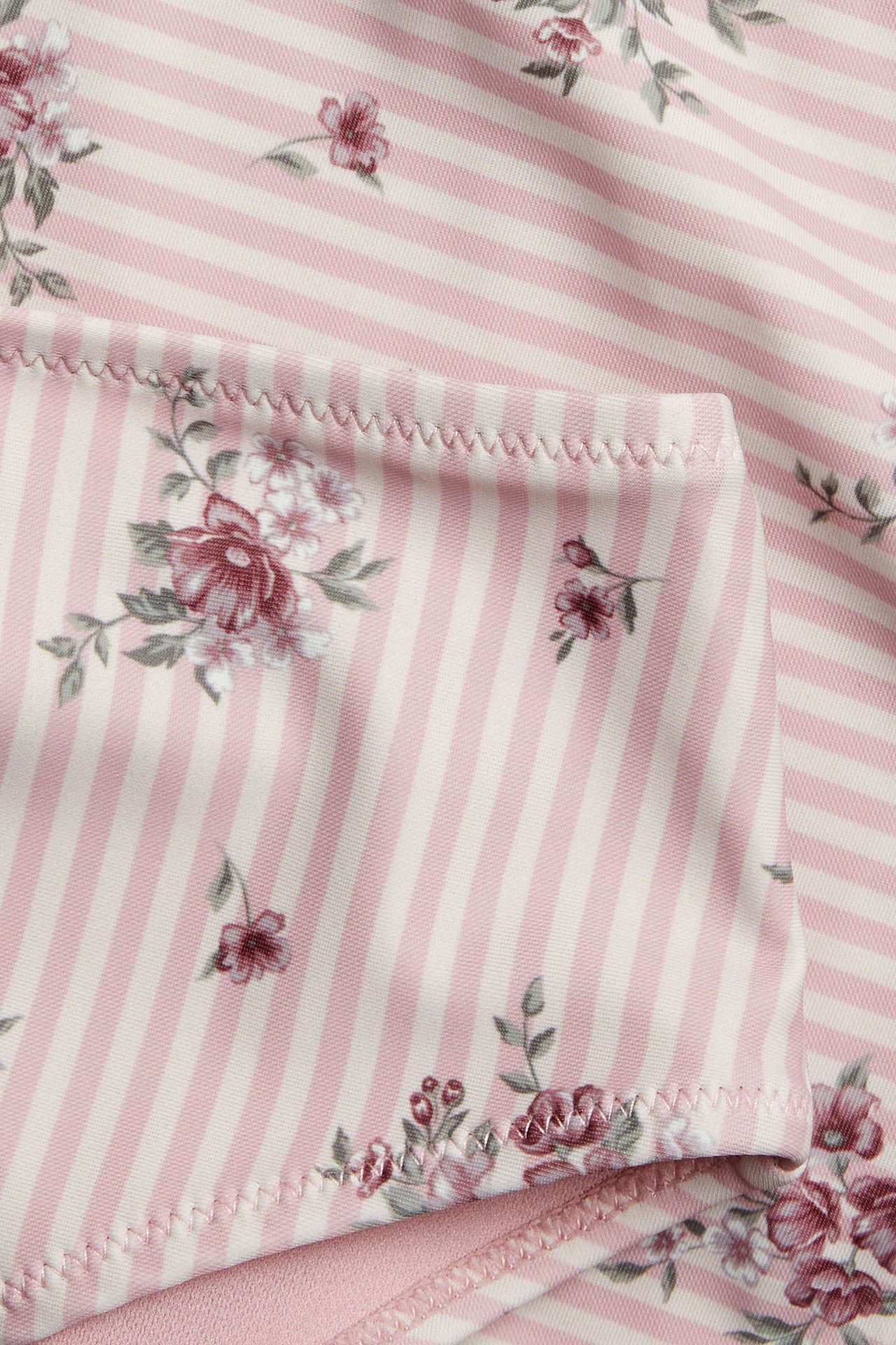 Nahaufnahme eines rosa-weiß gestreiften Stoffes mit Blumenmuster und Zickzack-Saum.