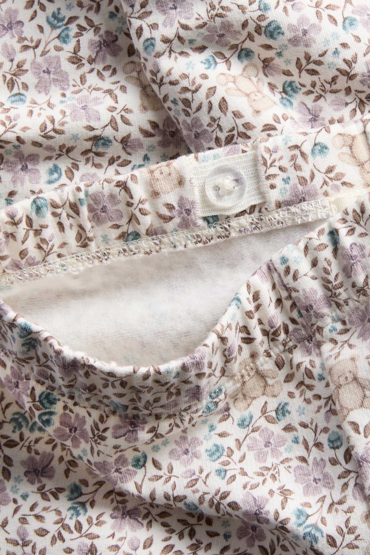 Nahaufnahme einer cremefarbenen Babyhose mit Blumen- und Bärendruck, verstellbarer Bund.