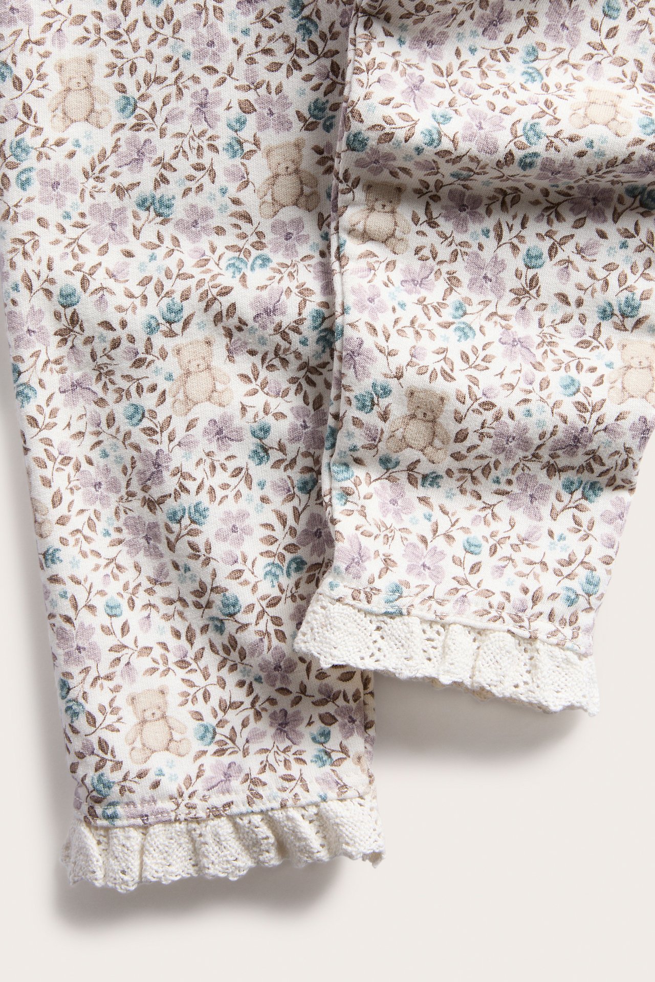 Nahaufnahme von cremefarbenen Leggings mit Blumen- und Teddybärenmuster mit weißer Spitze.