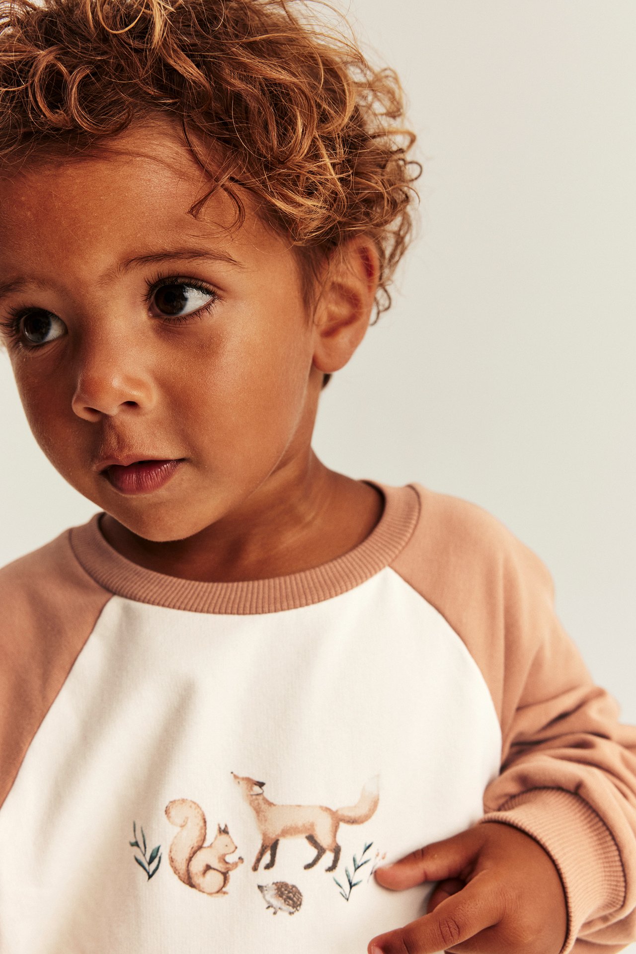 Front view of a kid wearing a two-tone light brown and off-white raglan sweatshirt with an animal print.