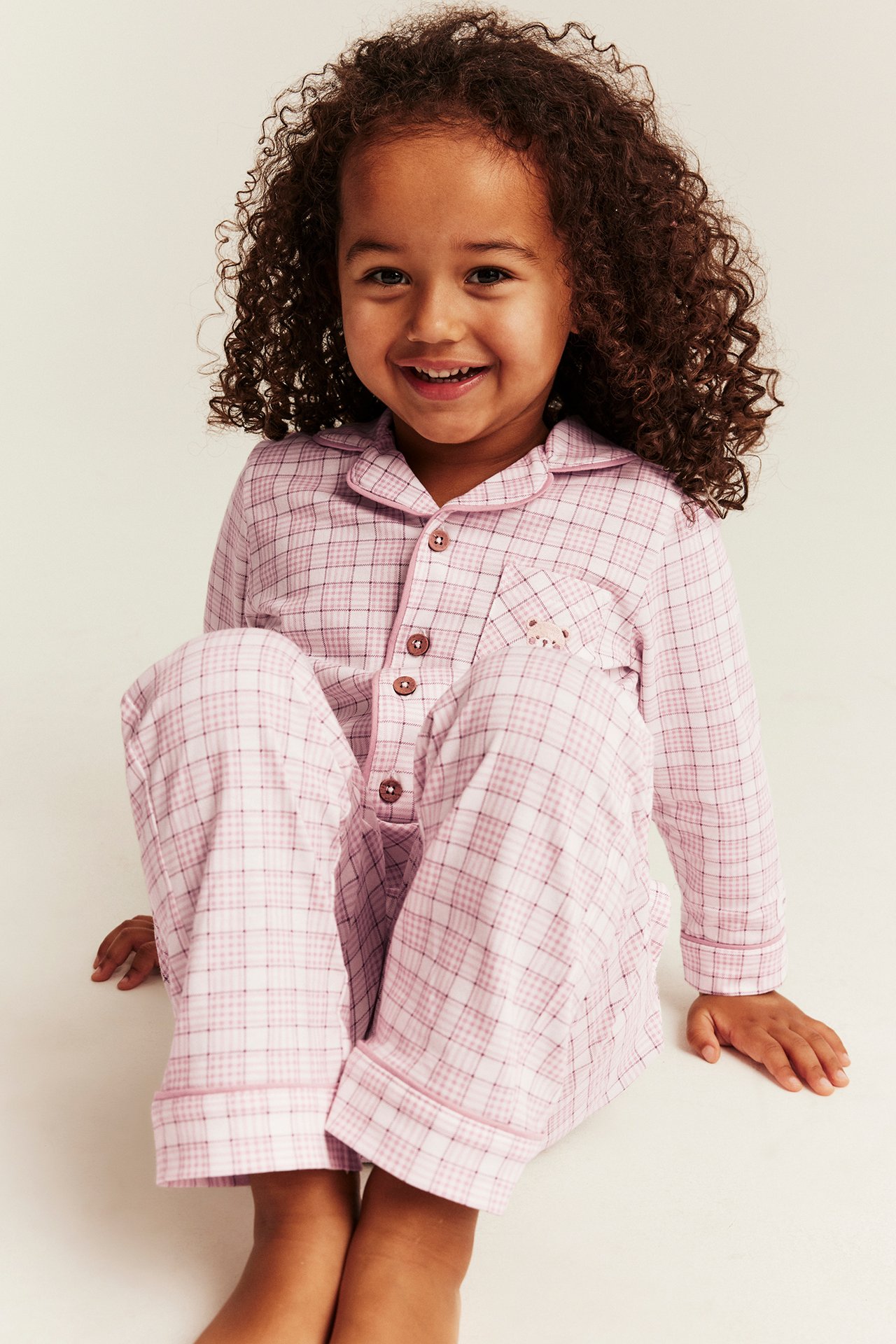 Front view of a kid wearing a pink and white plaid pajama set with a button-front top.