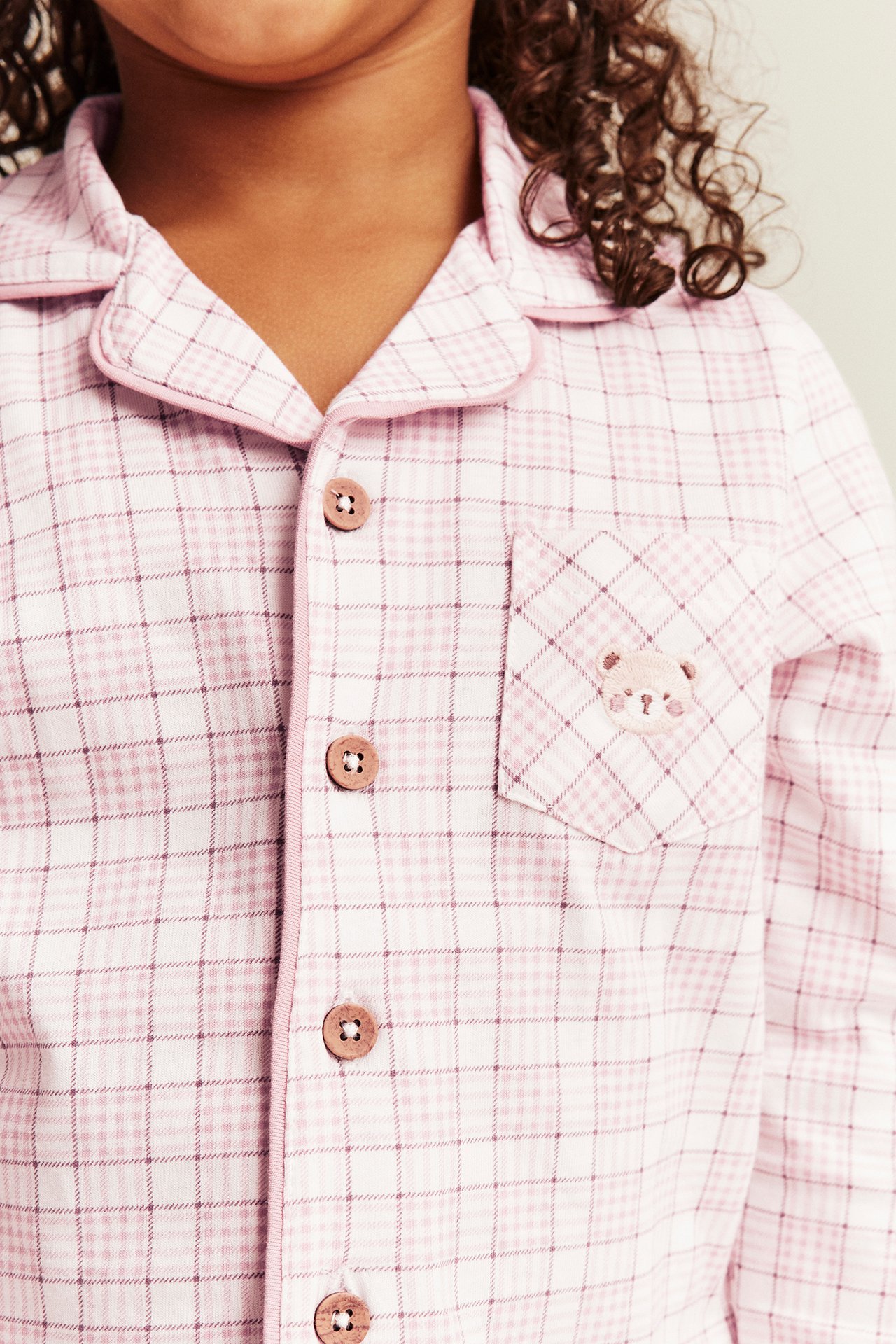 Close-up of a kid's pink plaid pajama top with wooden buttons and an embroidered bear pocket.