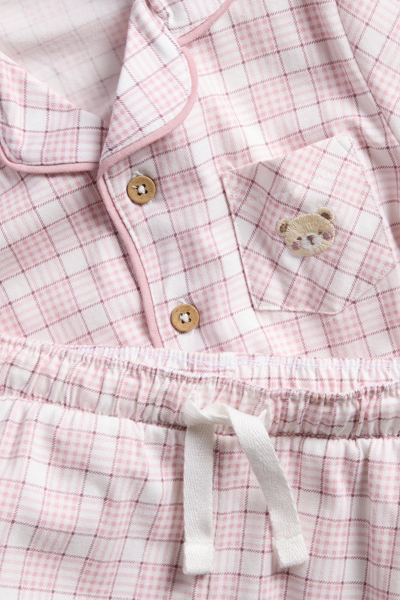 Close-up of a pink and white plaid pajama set with wooden buttons and an embroidered teddy bear.