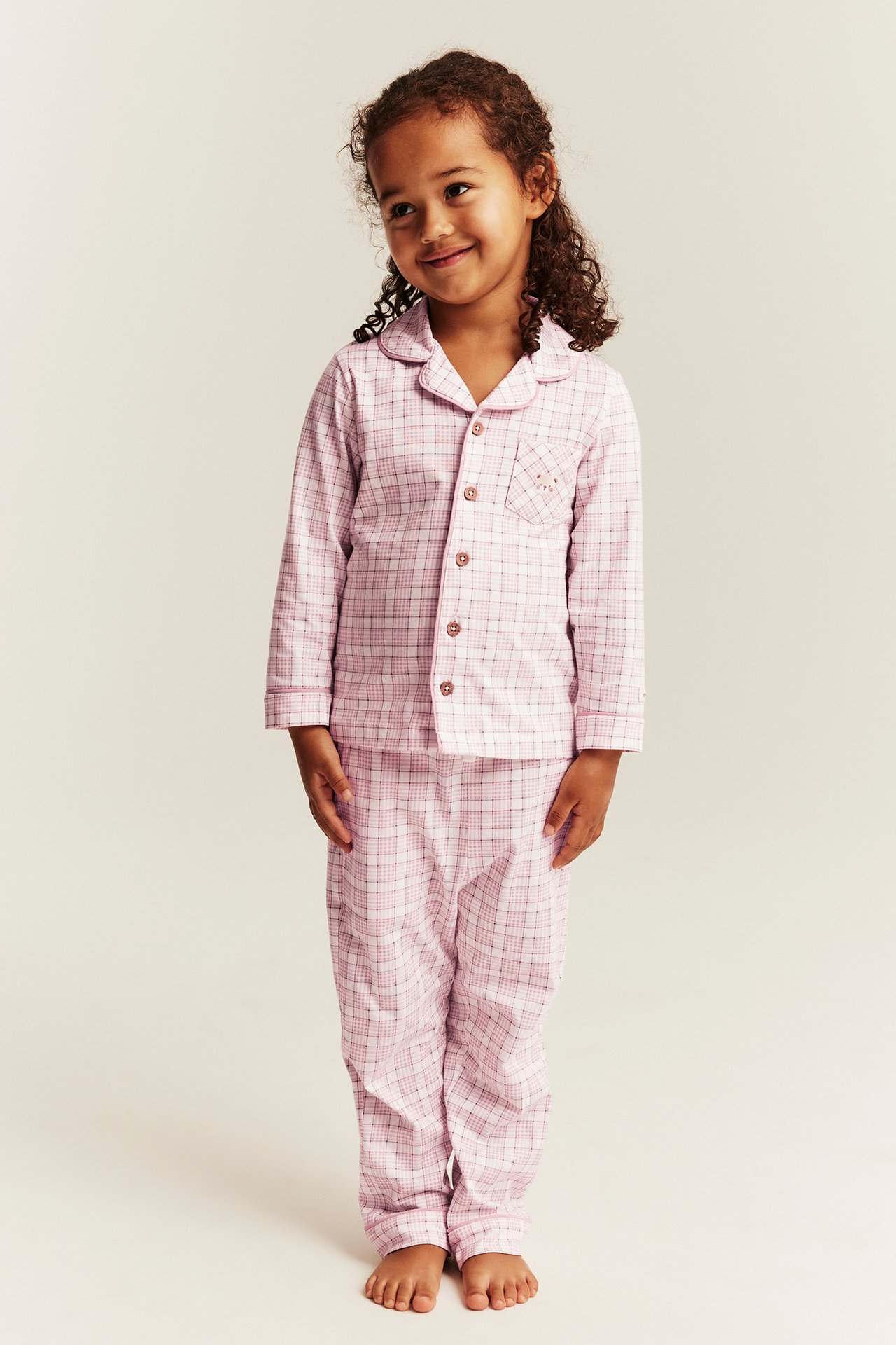 Front view of a kid wearing a pink plaid long-sleeved pajama set with buttons.