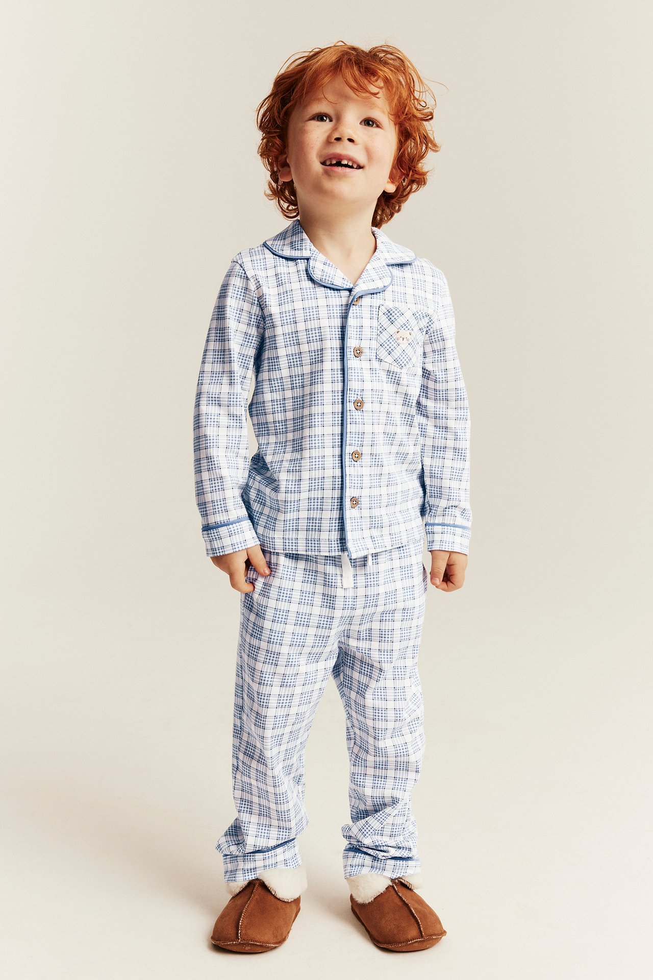 Front view of a kid wearing blue and white plaid pajamas and brown slippers.