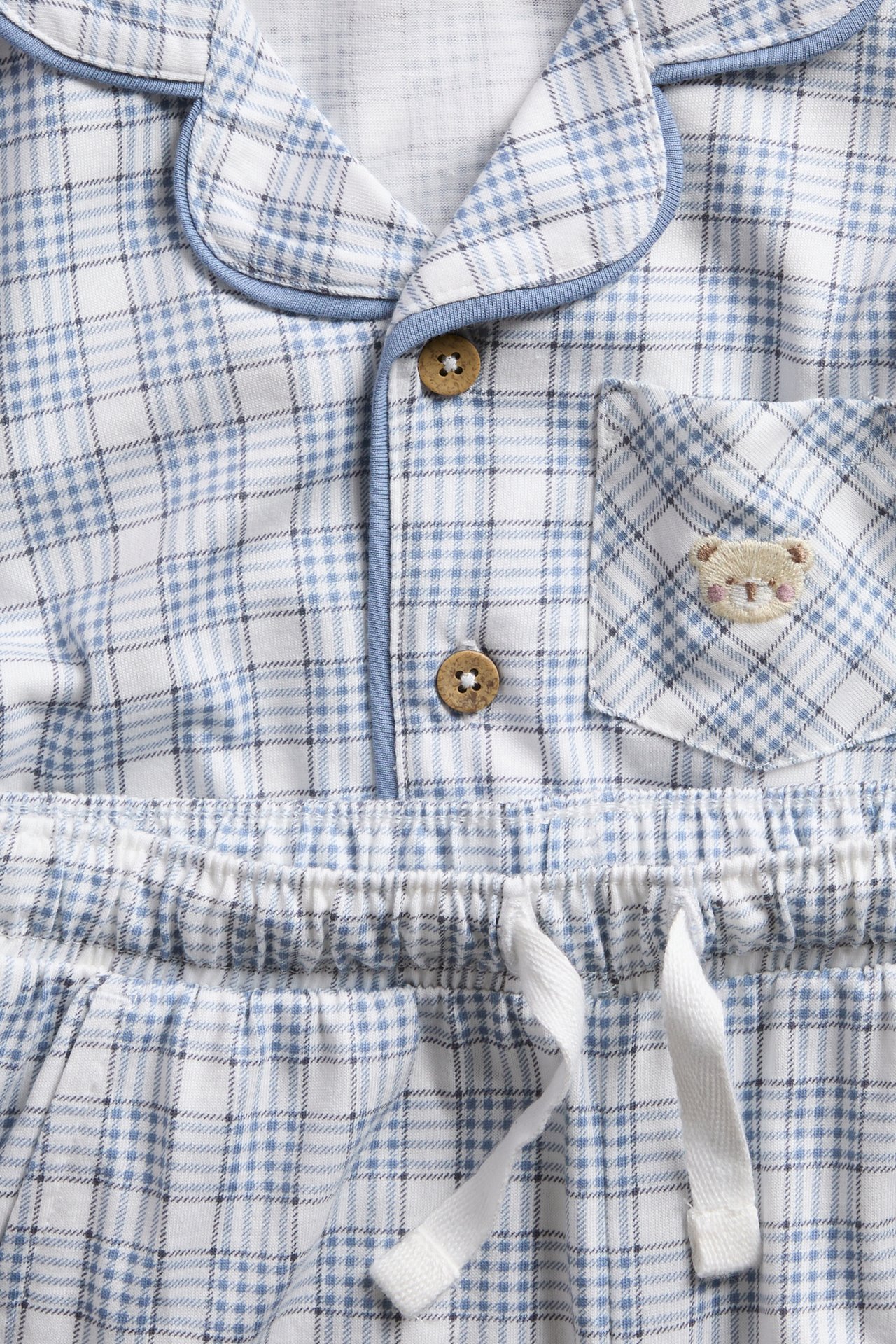 Close-up of a baby's blue and white plaid pajama set with a teddy bear embroidery.