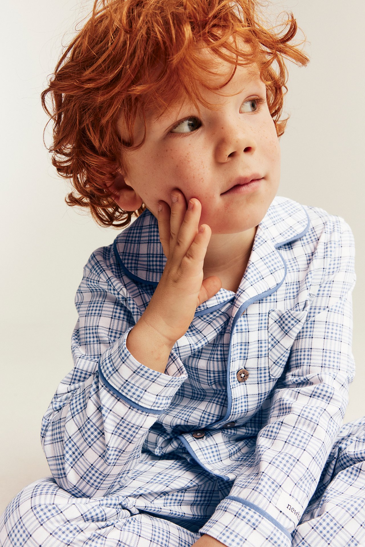 Close-up of a kid wearing a blue and white plaid long-sleeve pajama set with buttons.