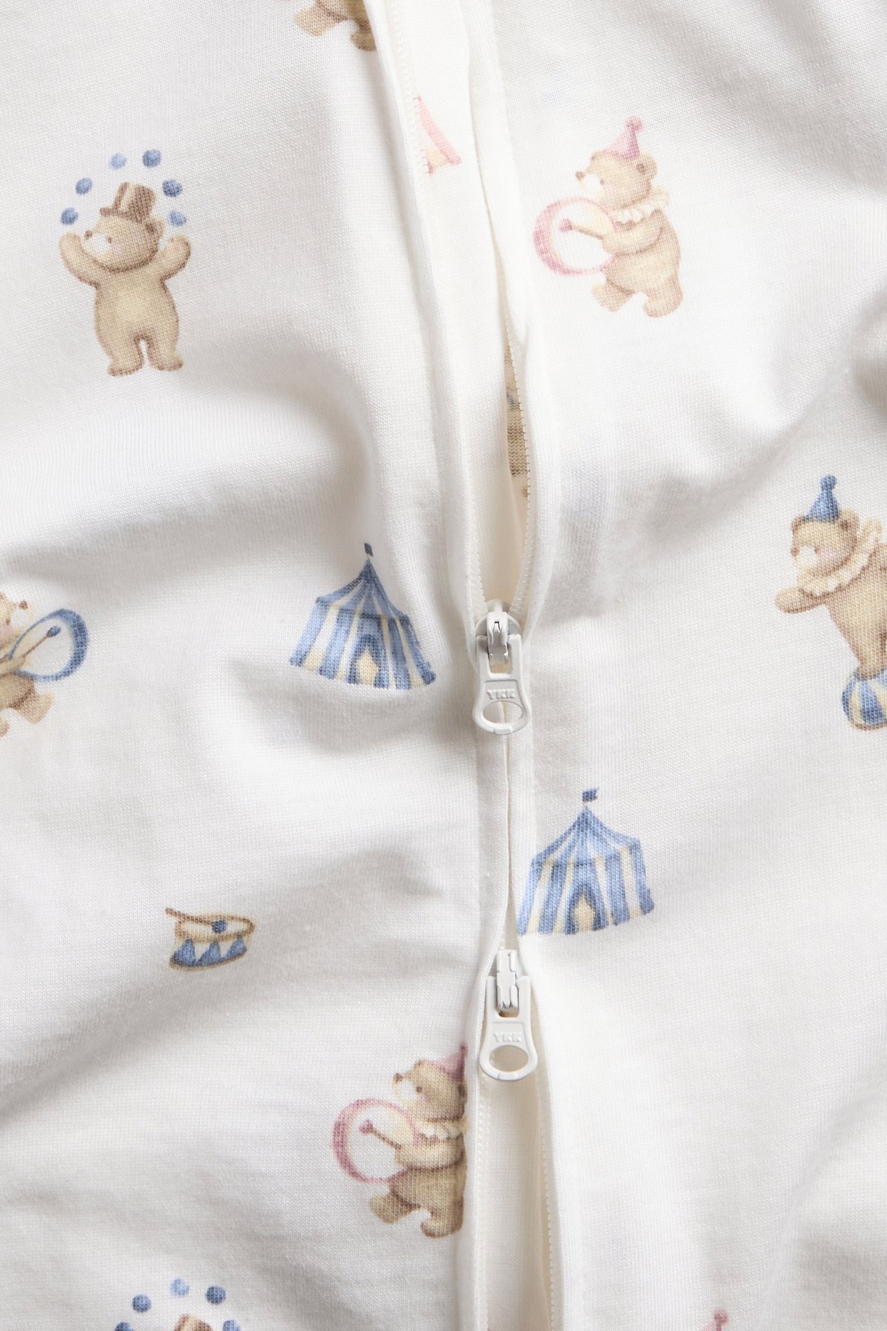 Close-up of a white baby garment with a circus print and zipper fastening.