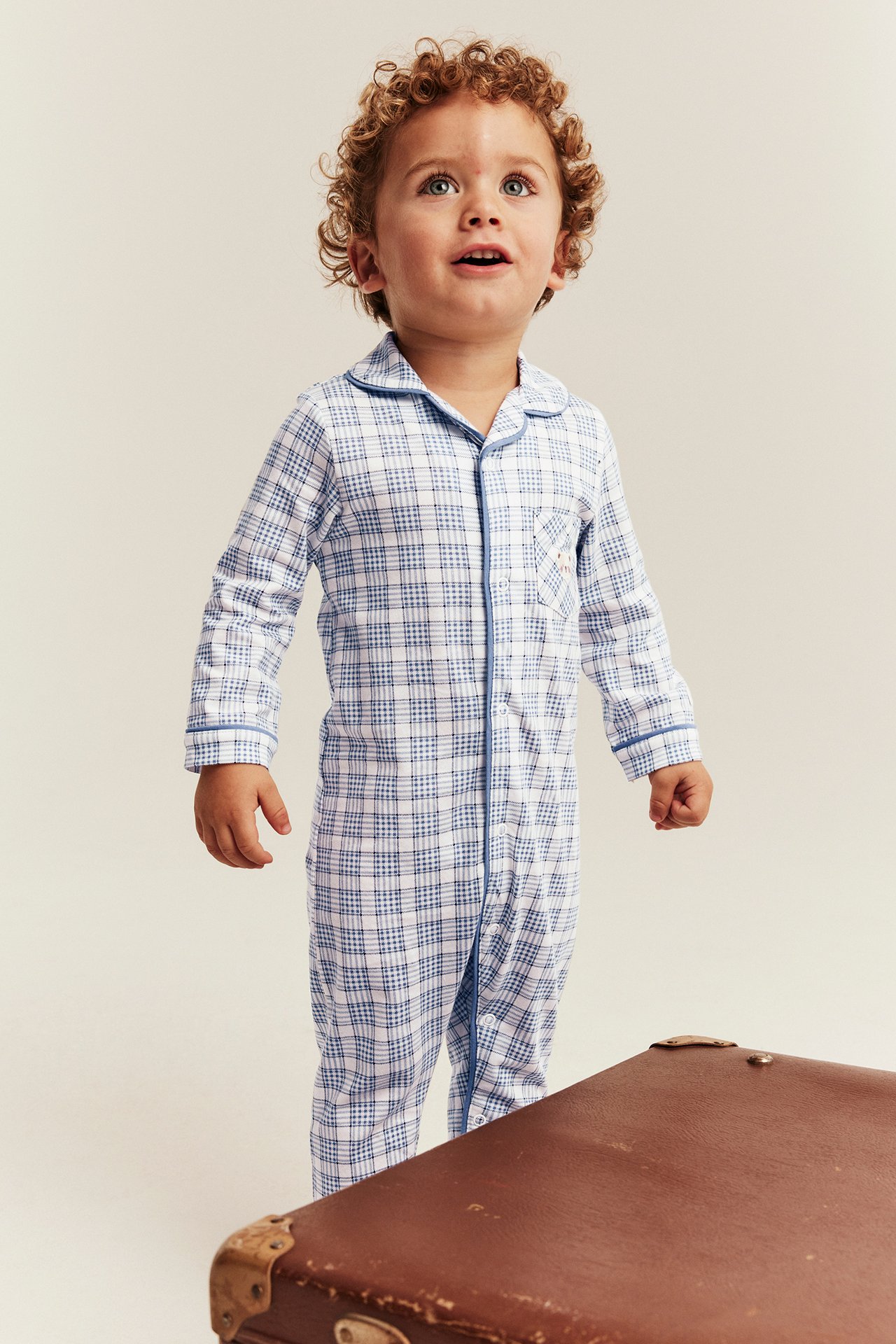 Vorderansicht eines Kindes in blau-weiß kariertem Einteiler-Pyjama mit Kragen und blauer Paspel.