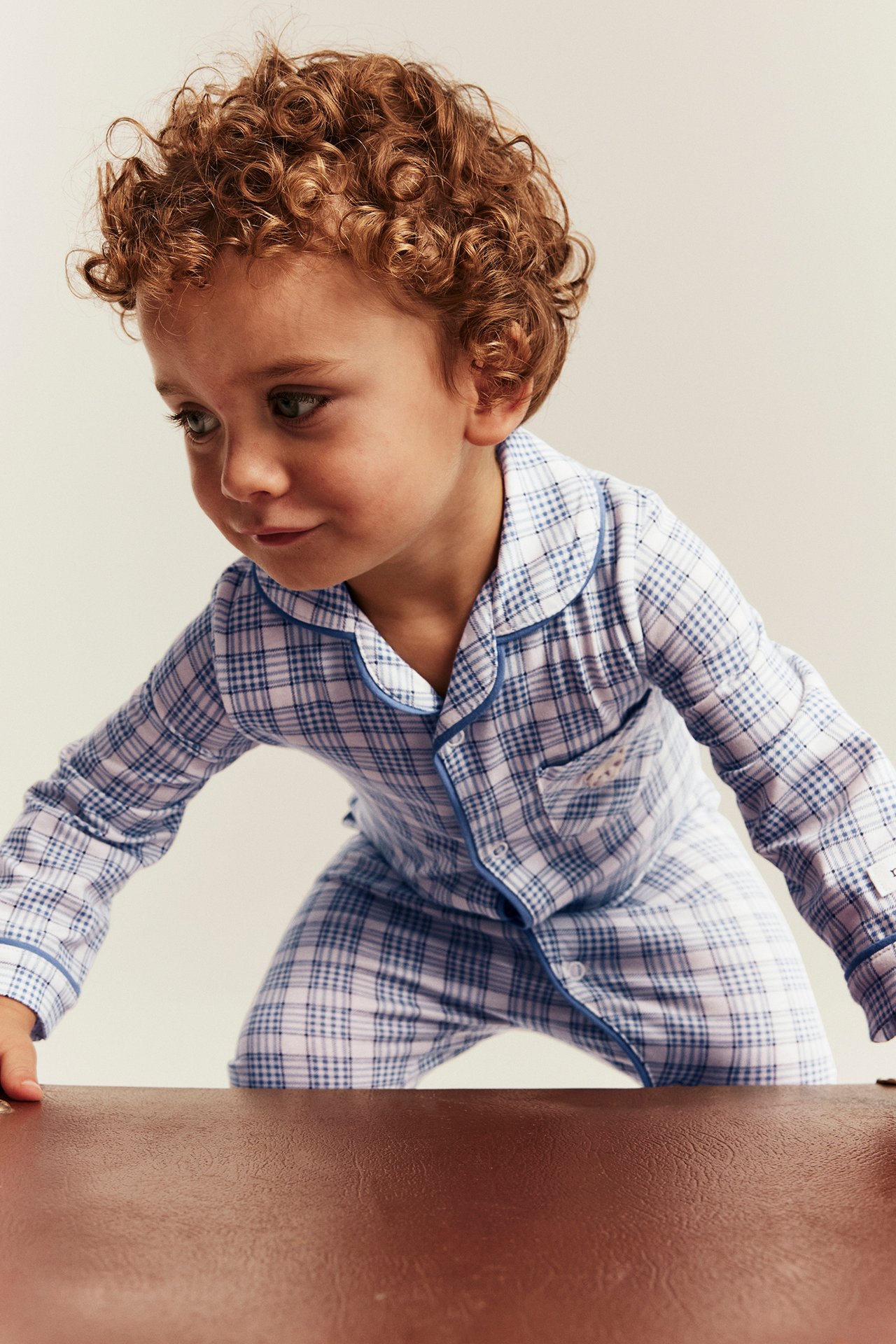 Vorderansicht eines Kindes in blau-weiß kariertem langärmeligem Pyjama mit blauer Paspelierung.