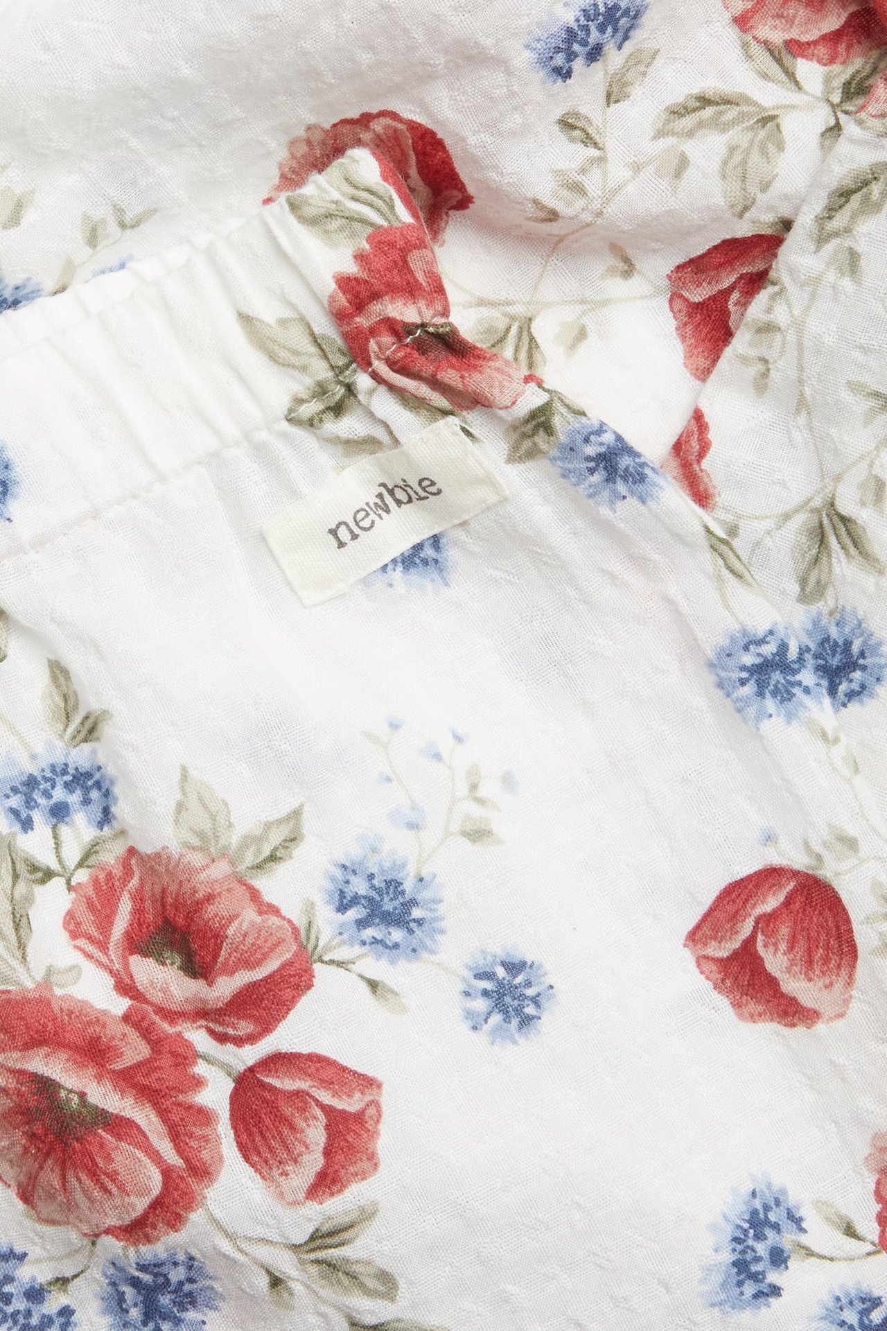 Close-up of a white baby garment with red and blue floral print, showing a 'newbie' label.