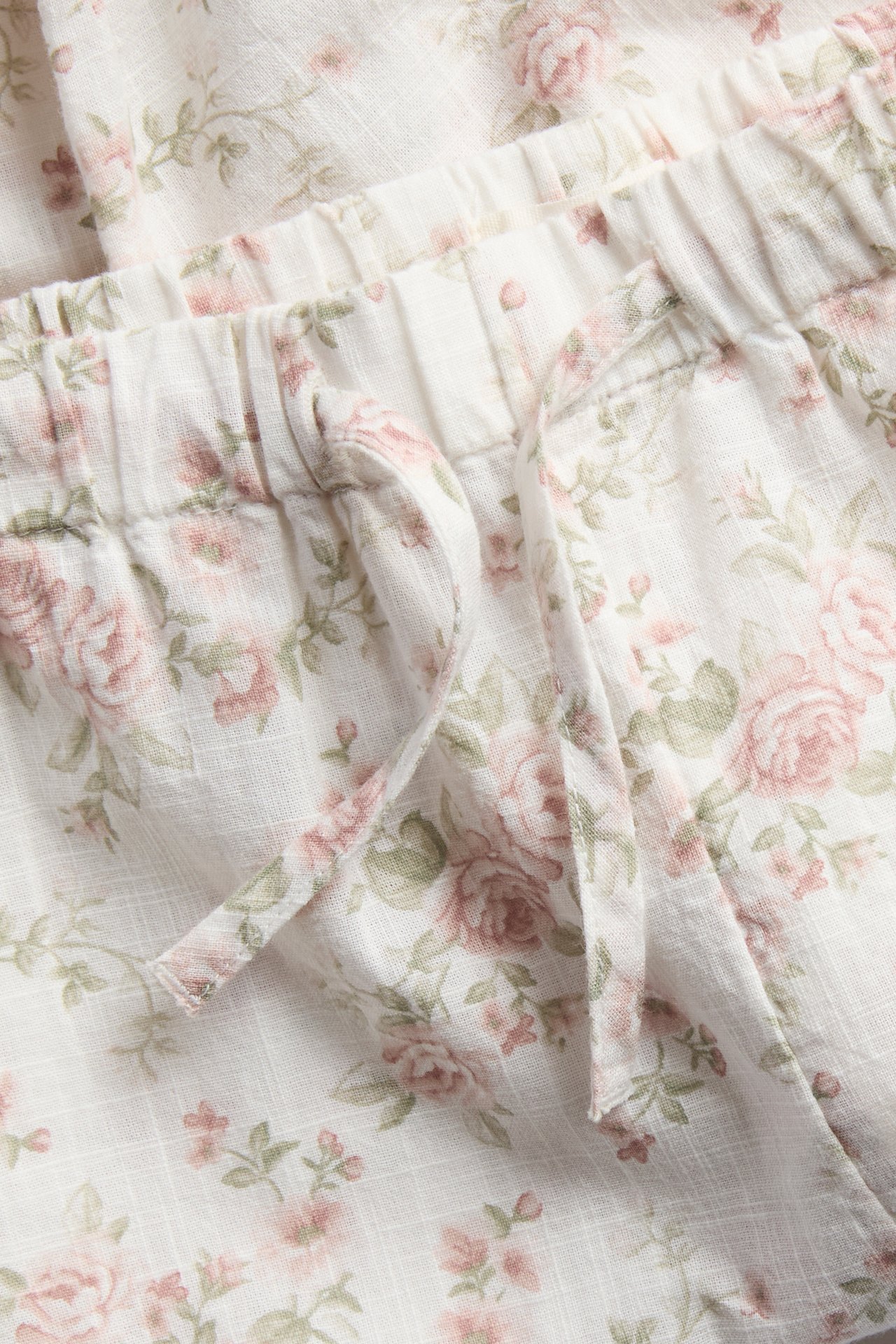 Nahaufnahme von weißen Shorts mit Blumenmuster, elastischem Kordelzugbund aus strukturiertem Stoff.