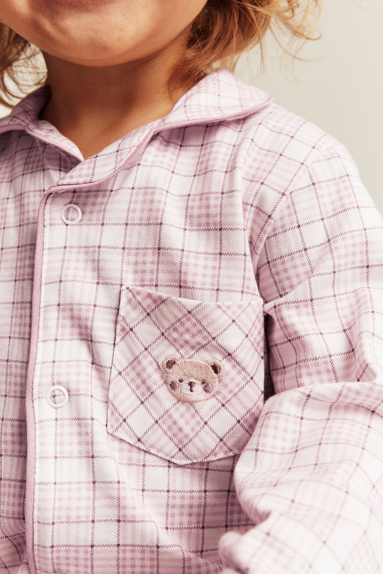 Close-up of a kid in a pink plaid pajama shirt with a teddy bear embroidery on the pocket.