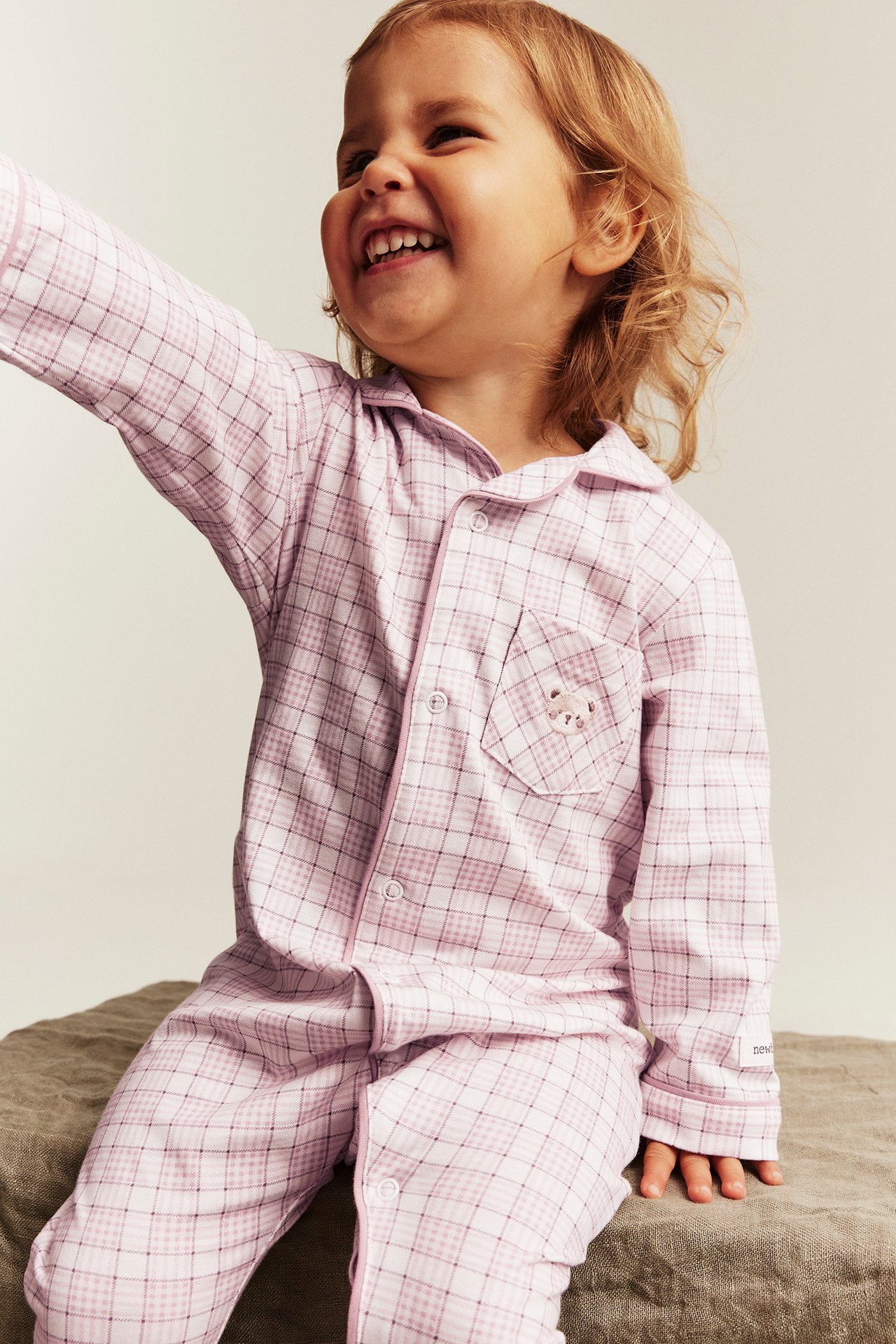 Front view of a kid wearing a pink and white plaid button-up pajama set with a bear embroidery.