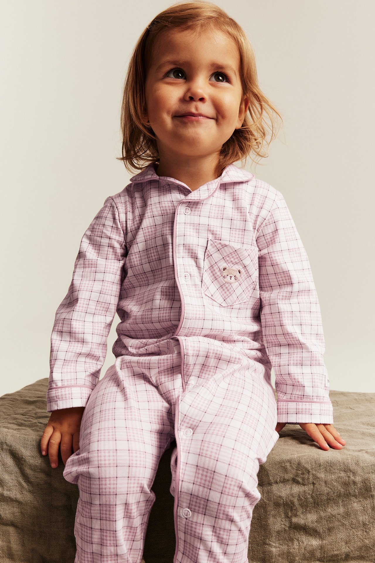 Front view: Kid girl wears pink plaid pajamas with a collar and an embroidered bear pocket.