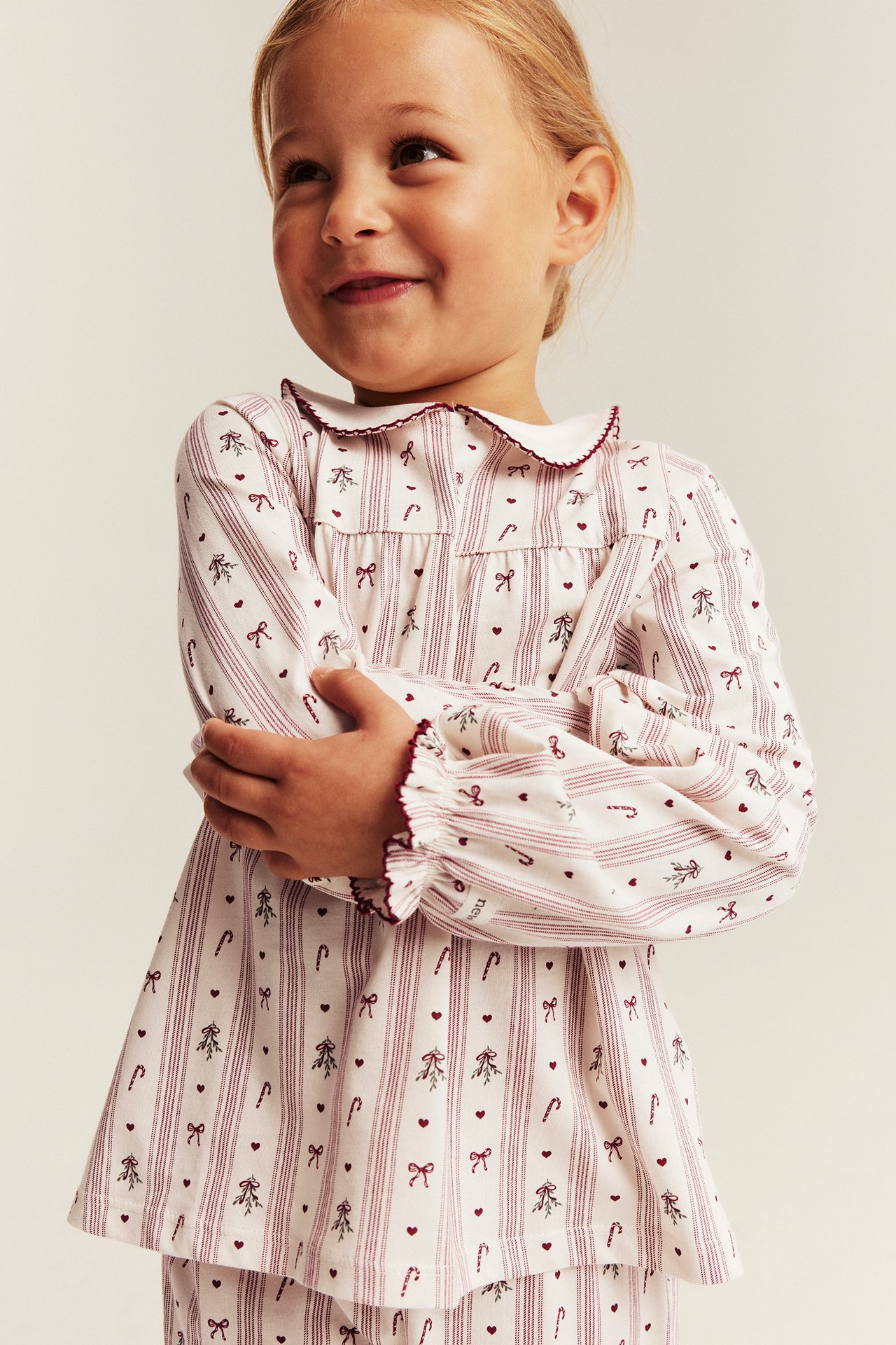 Vorderansicht eines weißen Kinder-Pyjamaoberteils mit roten Streifen, Weihnachtsdruck und Rüschendetails.