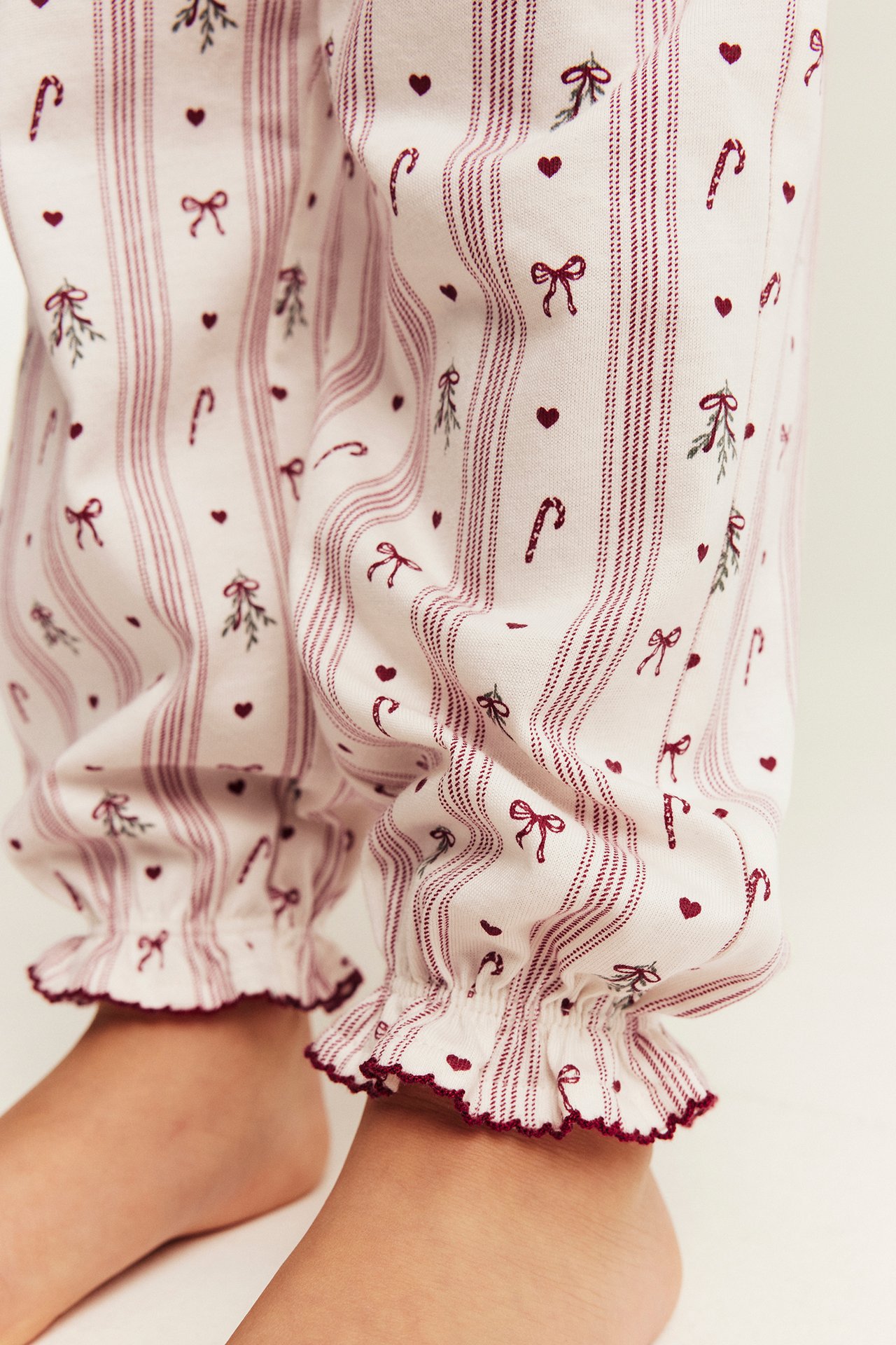 Nahaufnahme von weißen Pyjamahosen mit roten Streifen, Herzen, Schleifen, Zuckerstangen und Rüschenbündchen.